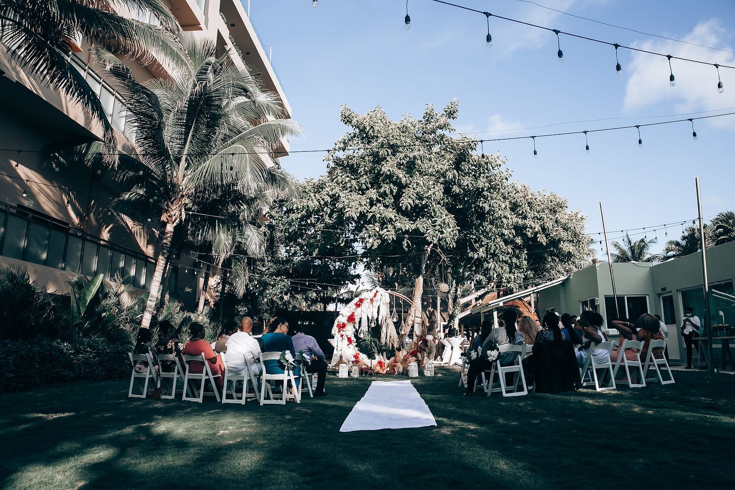 String lights illuminate an outdoor wedding reception venue with palm trees and framed photos hanging between trees.