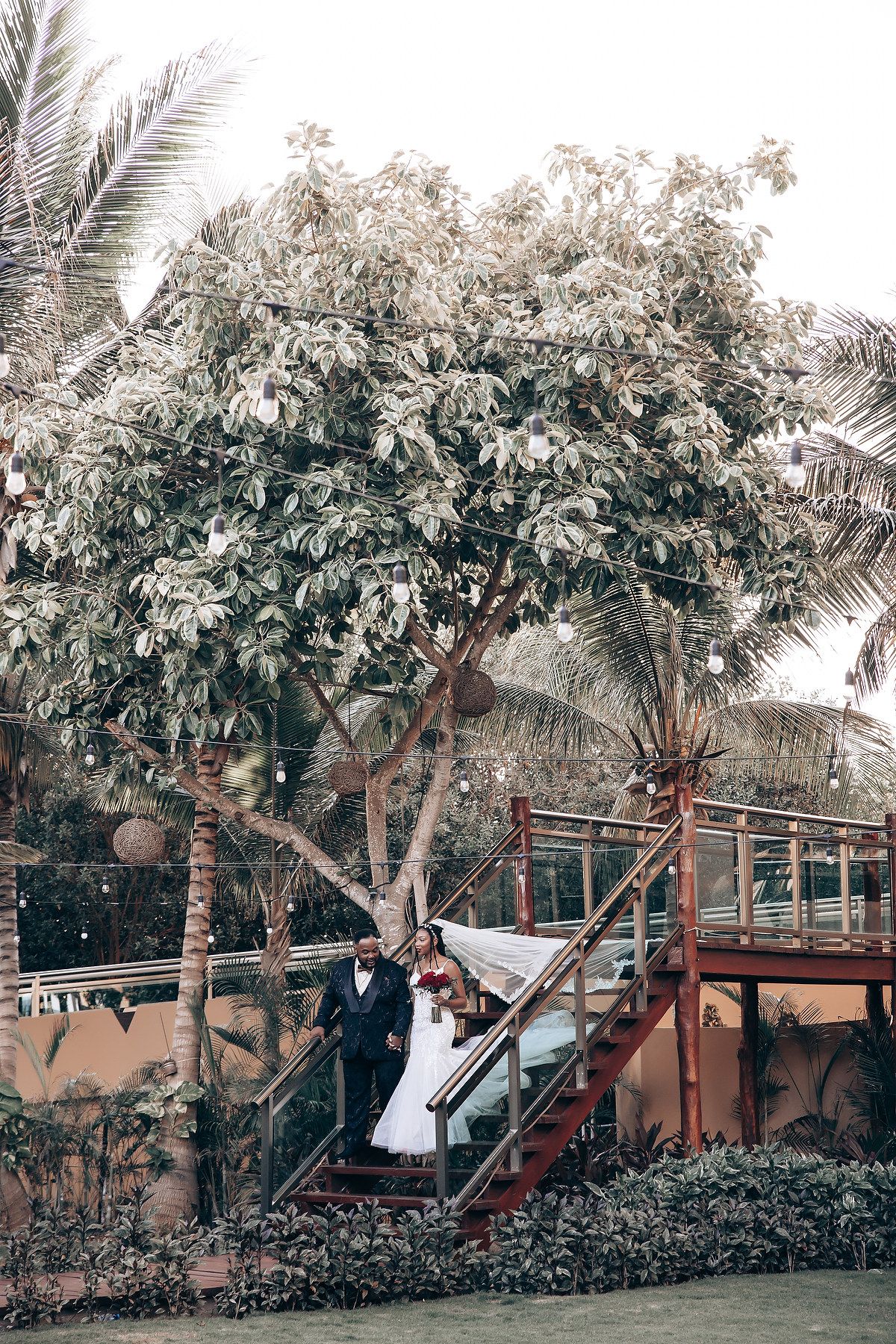 Wedding party poses on a rustic wooden deck surrounded by lush tropical palm trees and greenery.