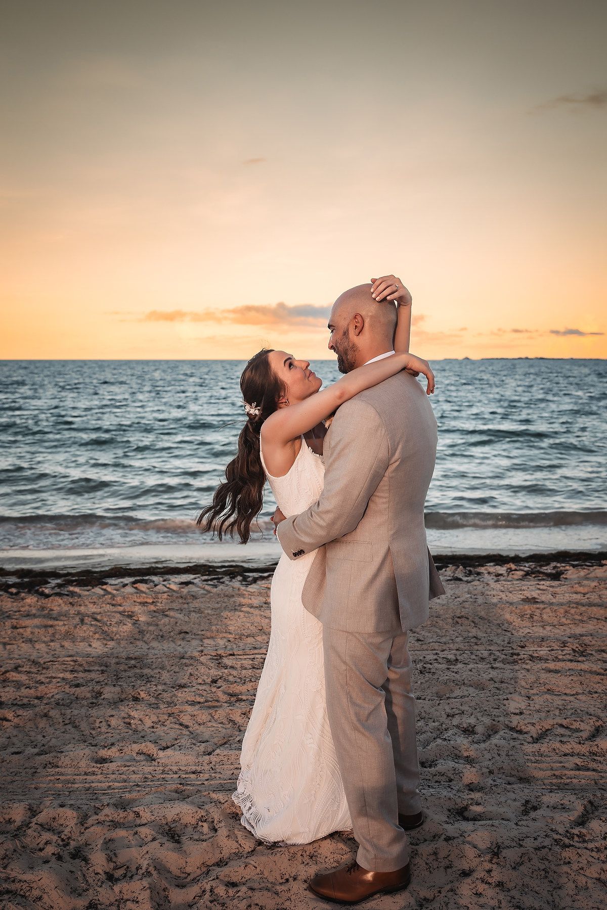 Newlyweds dance romantically on the beach at sunset with ocean waves in background.