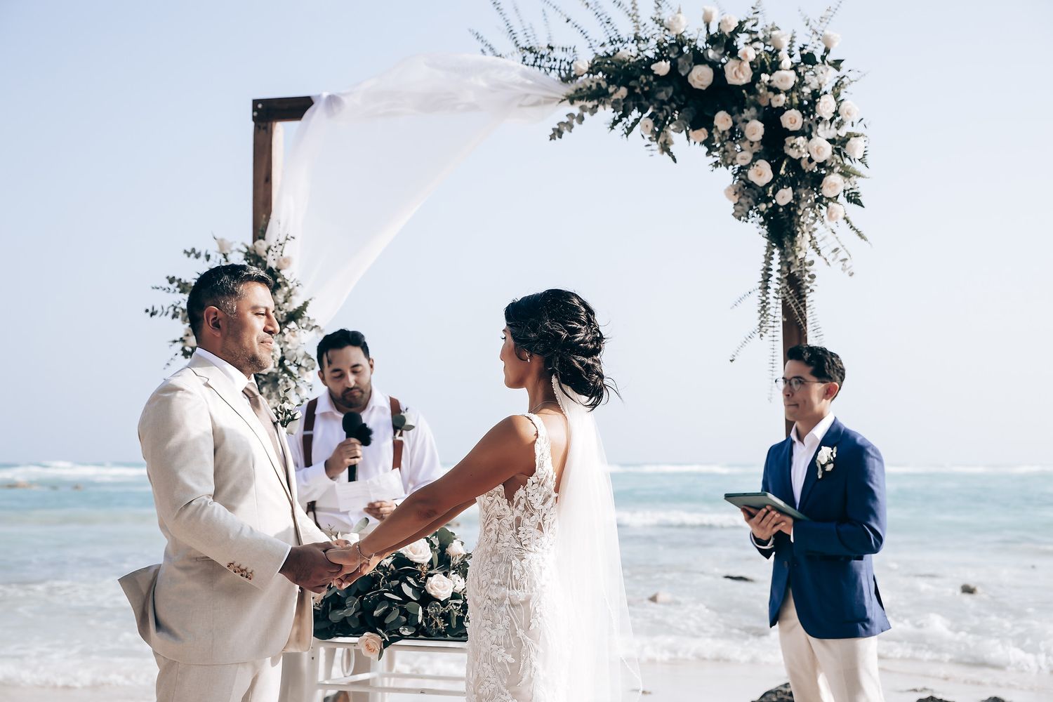 Romantic beach wedding ceremony with palm trees and ocean waves in the background.