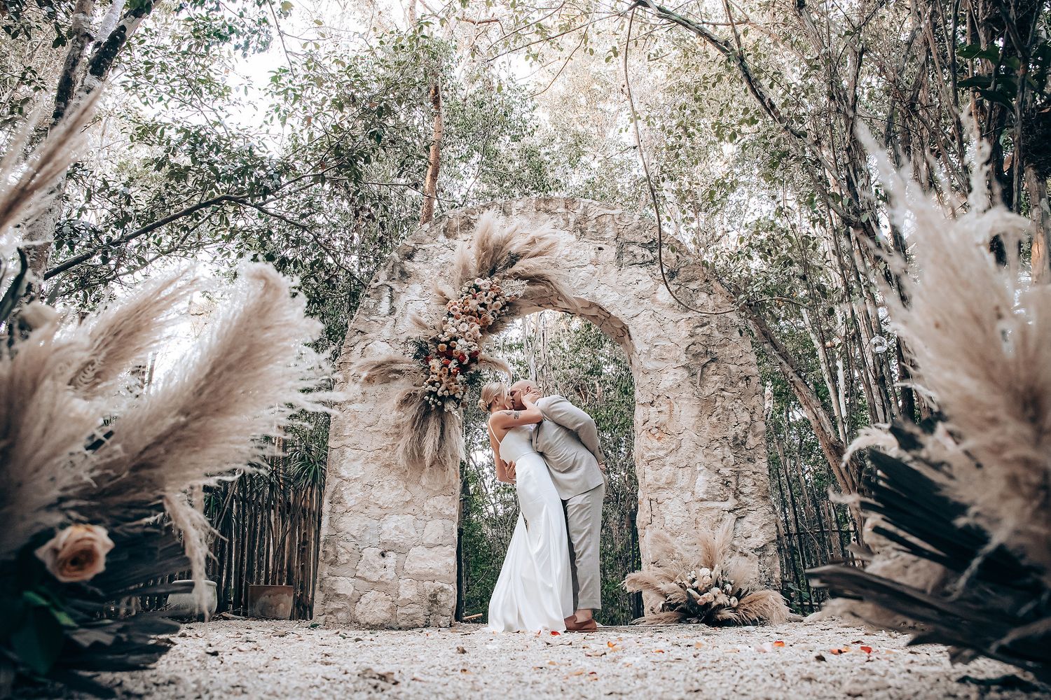 Romantic outdoor wedding ceremony setting with dried floral arrangements and natural woodland backdrop.
