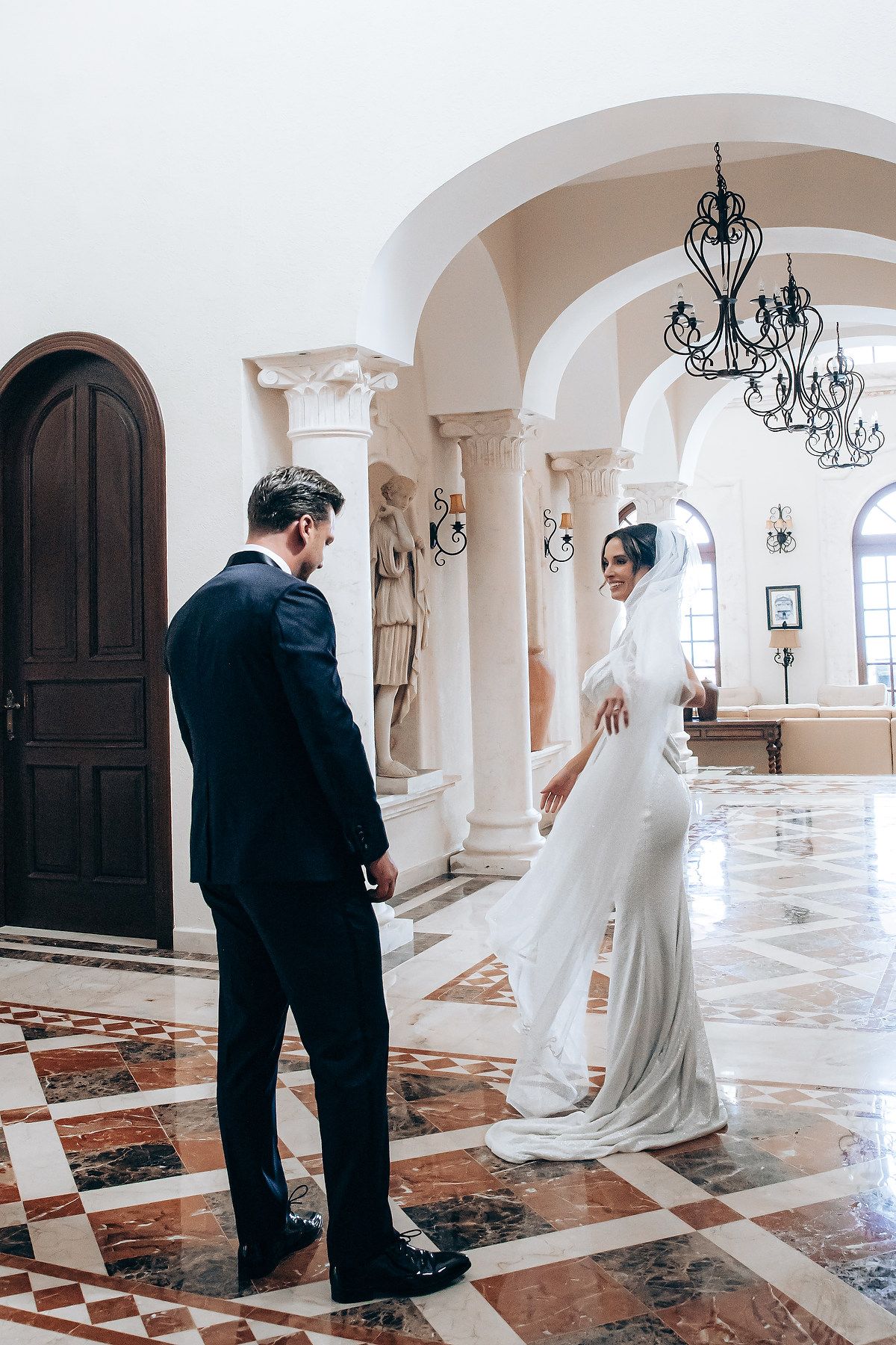 A wedding couple poses in an elegant church interior with marble columns and arched windows.