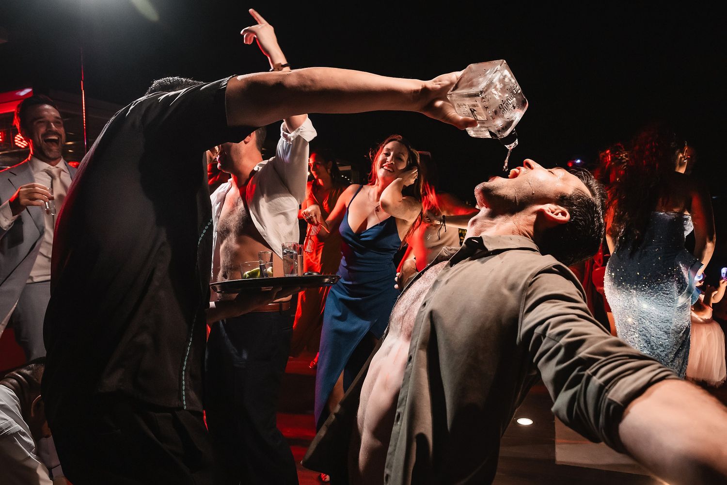 People dancing and celebrating with expressive movements in a dark venue setting.