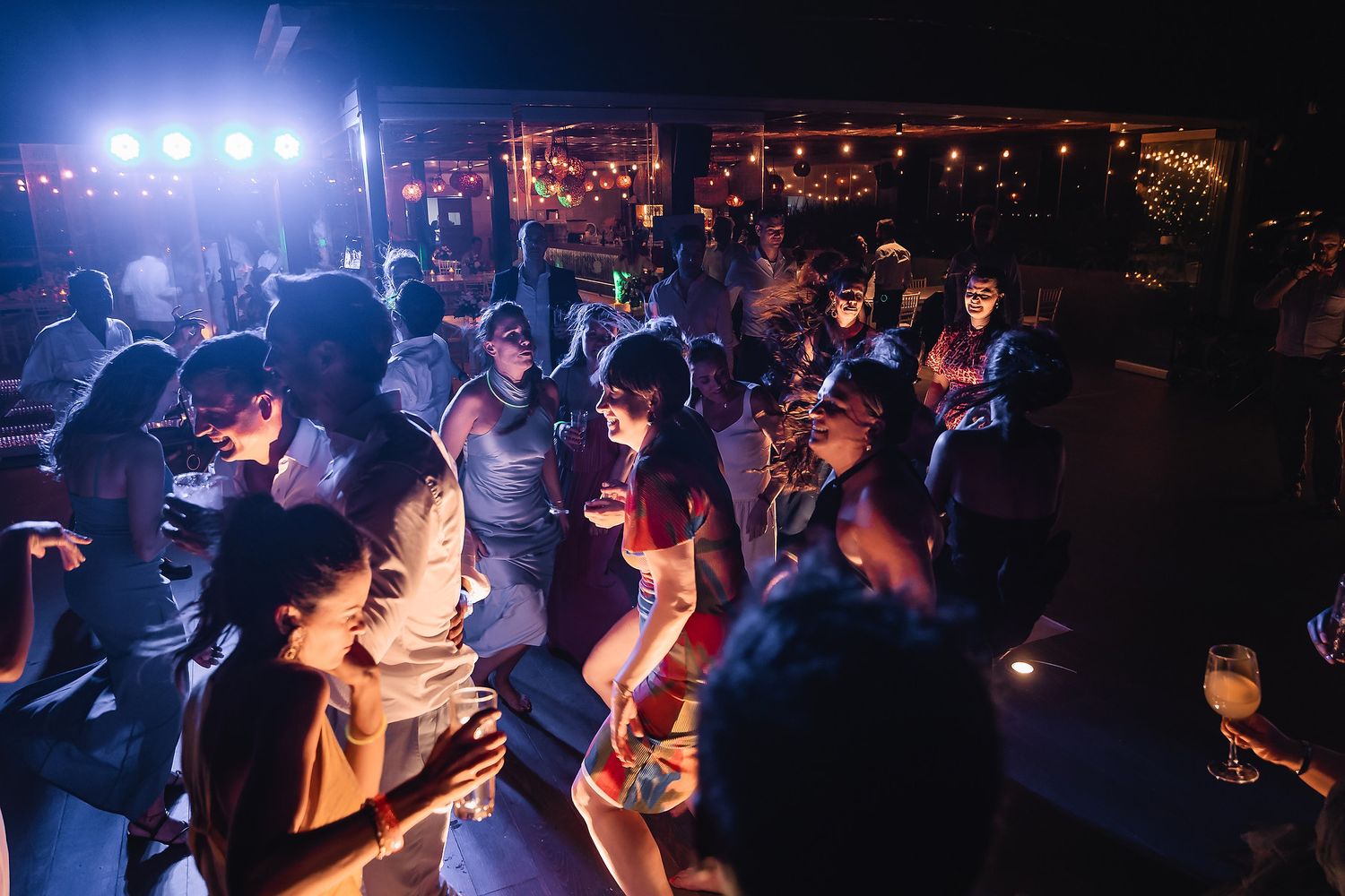Crowded dance floor at a nighttime wedding reception with blue atmospheric lighting.
