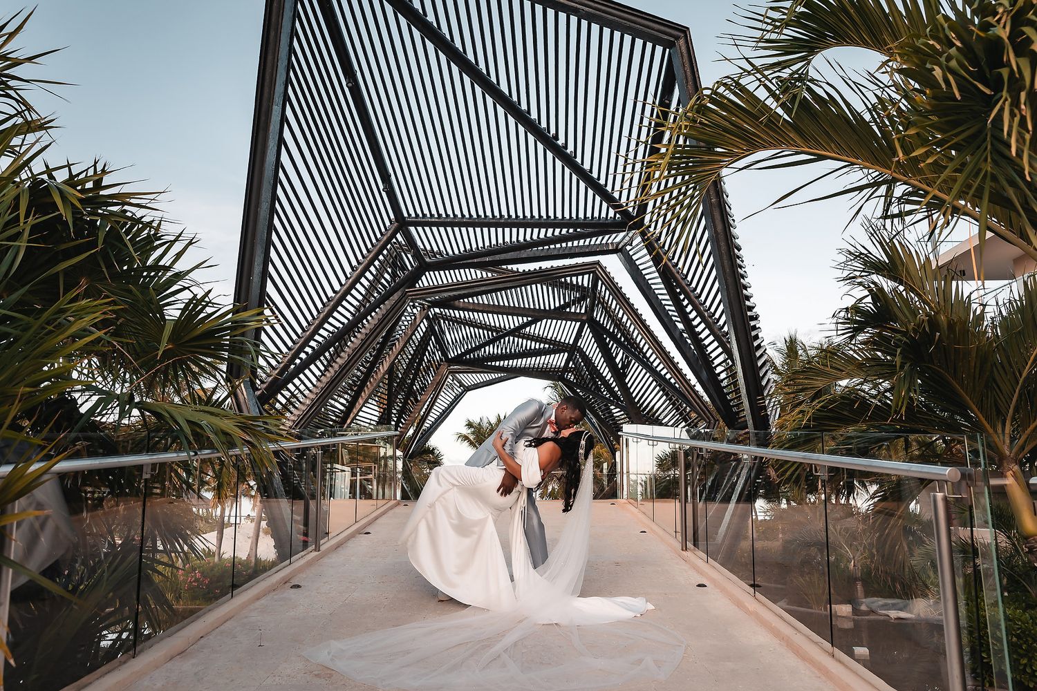 Dramatic wedding photo in a modern geometric bridge walkway surrounded by palm trees.