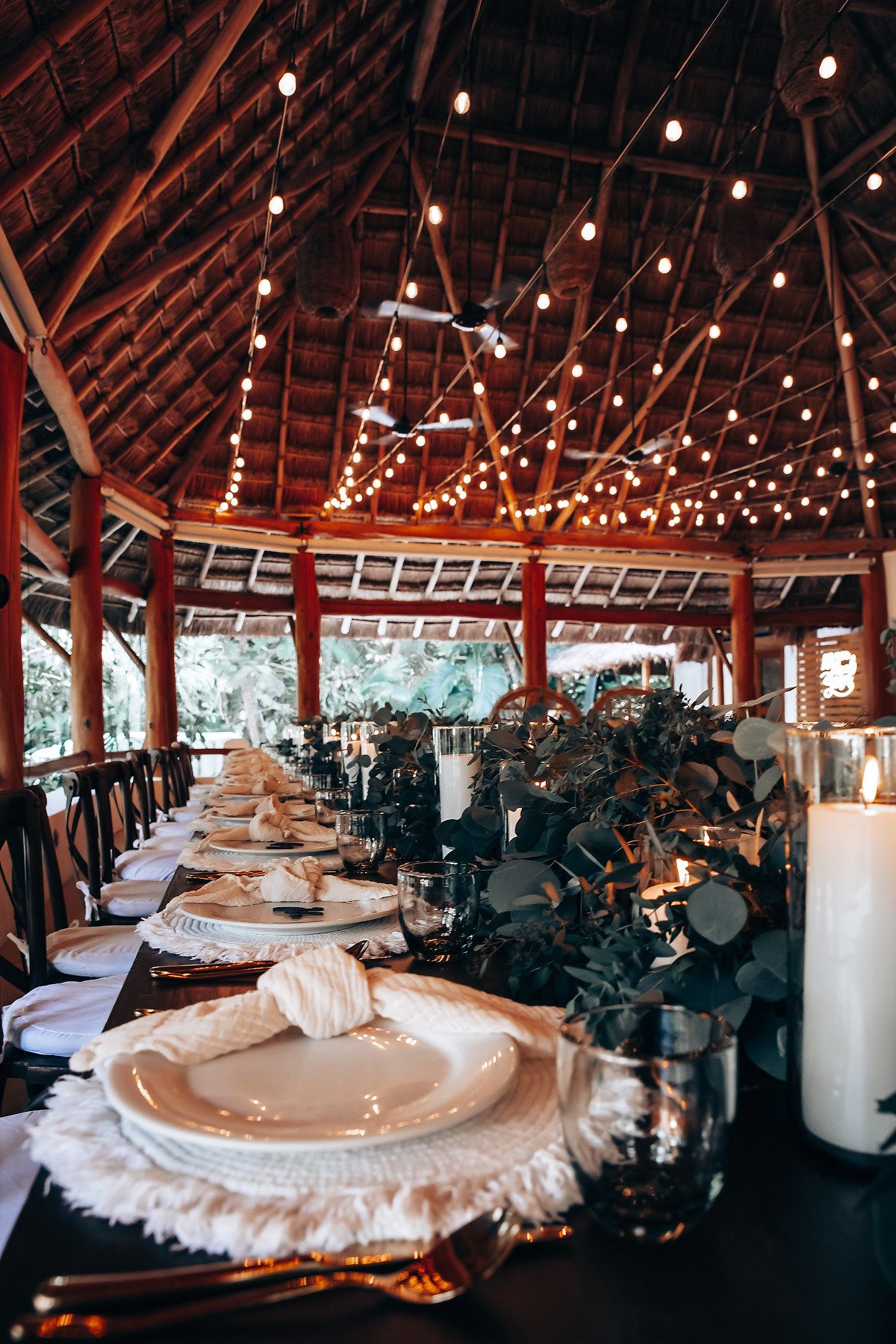 Elegant wedding reception table setting with string lights in a rustic wooden pavilion.