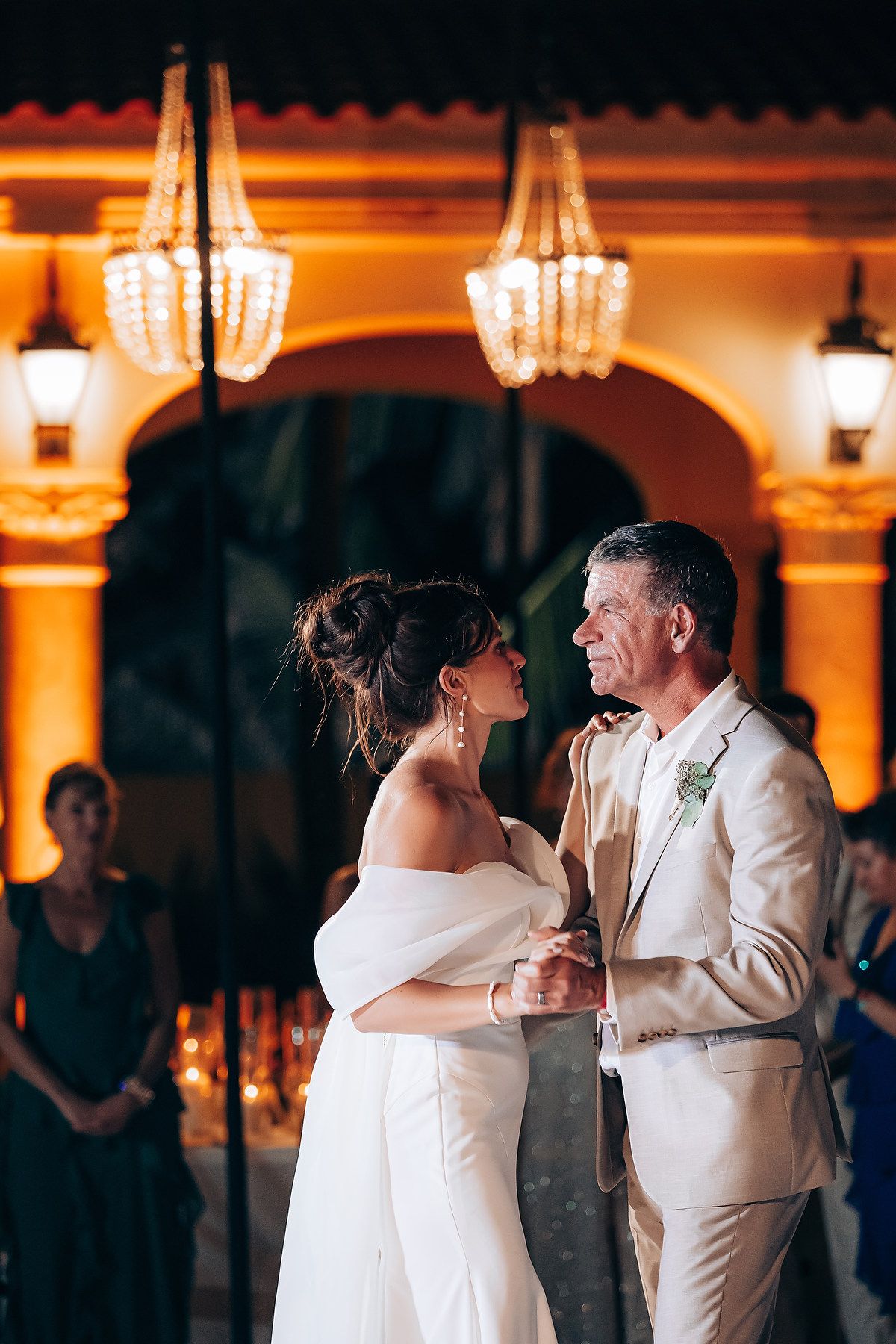 Elegant wedding dance captured in a warmly lit ballroom with ornate chandeliers.