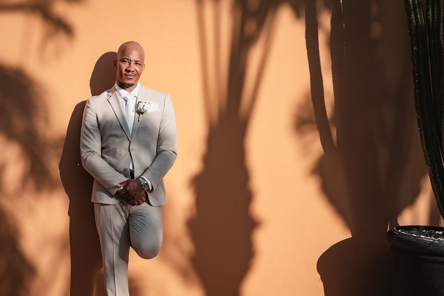 Wedding couple poses against a peach wall with dramatic palm tree shadows.
