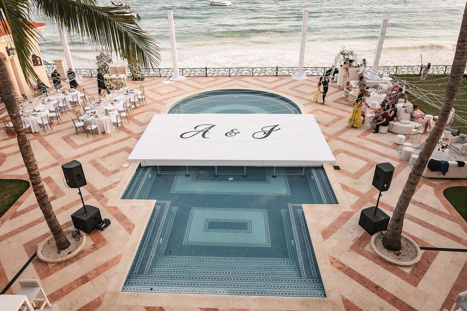 Aerial view of a resort pool deck with geometric tile patterns and palm trees.