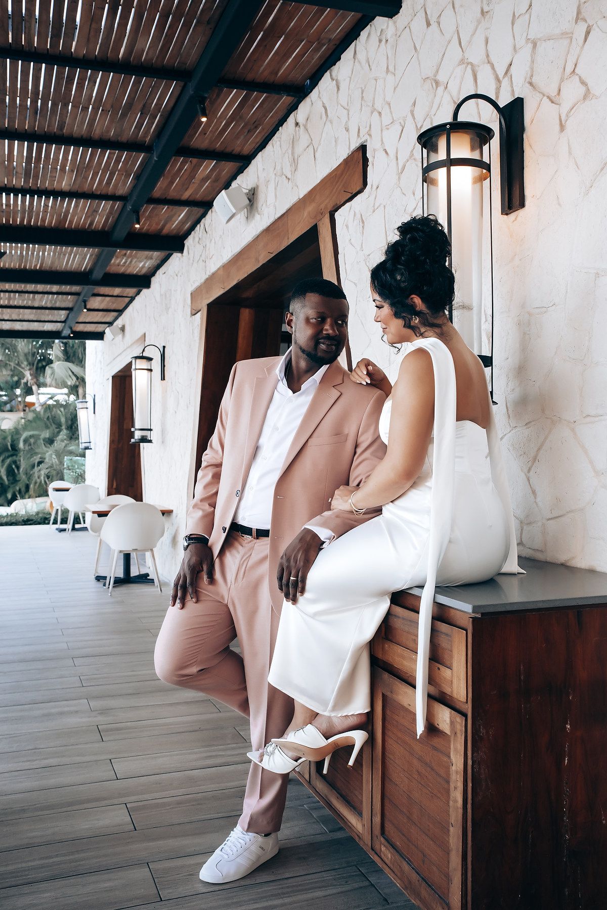 A couple in coordinated formal wear poses casually on an outdoor patio.