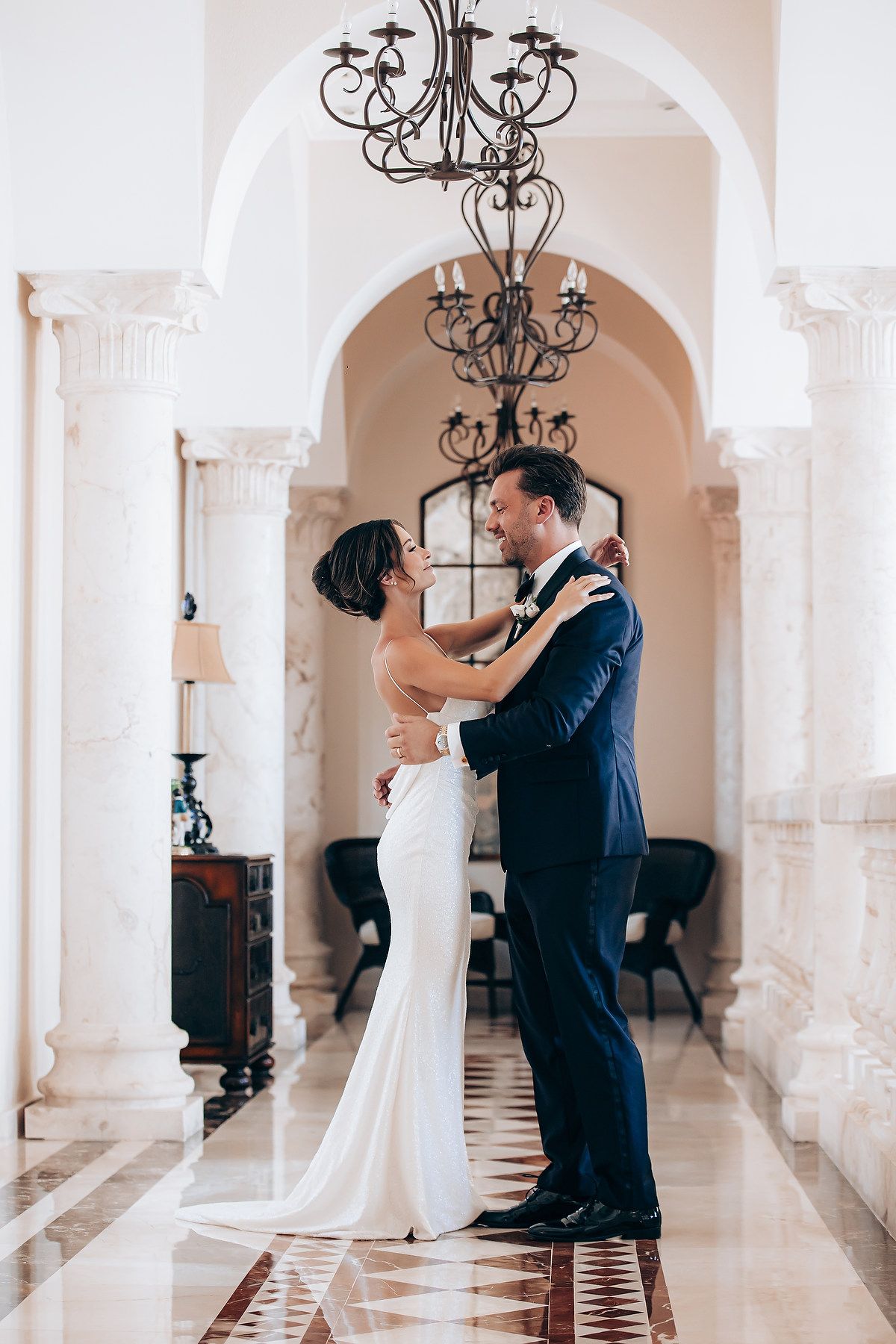 A romantic moment captured between a couple dancing under ornate archways and chandeliers in a luxurious venue.
