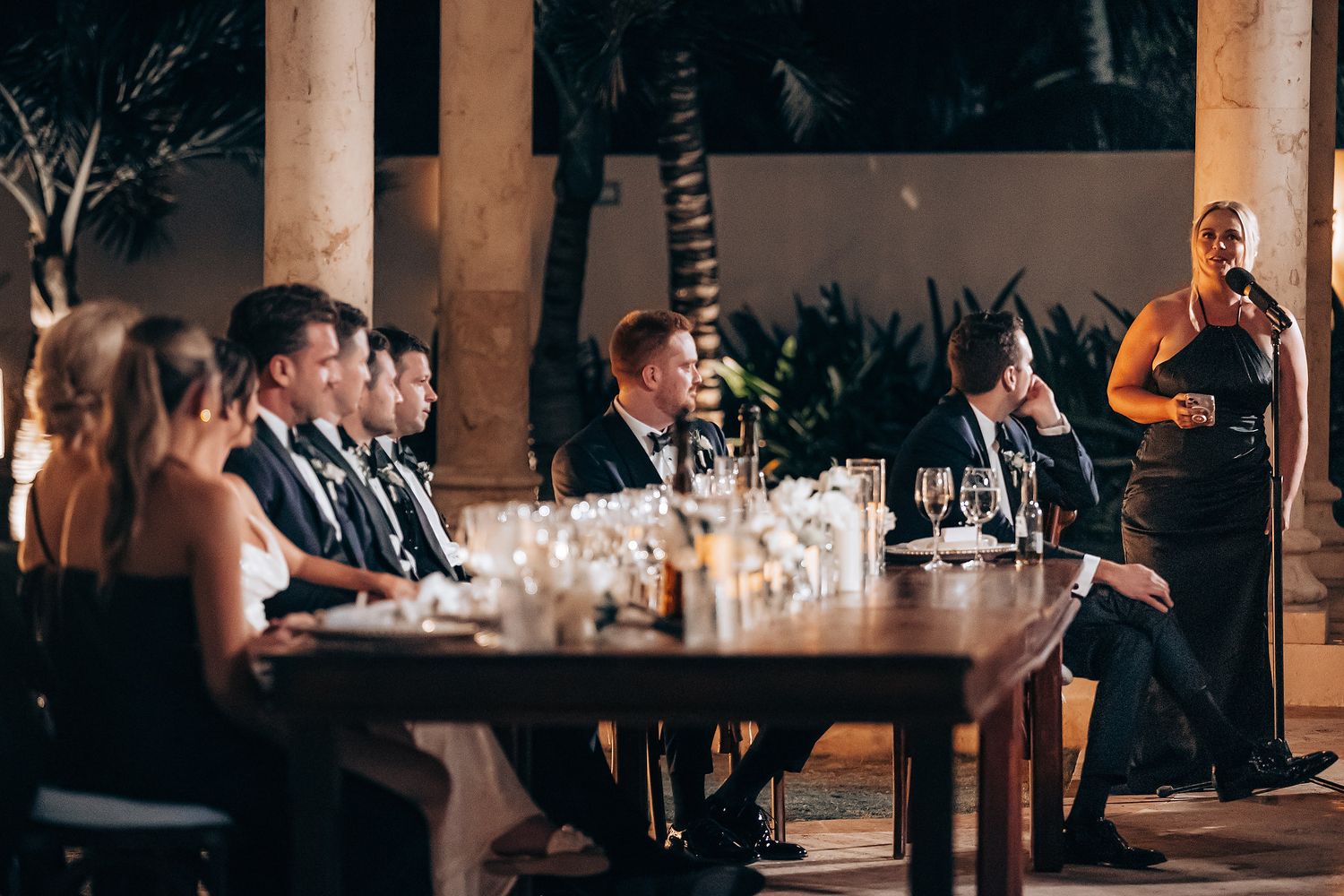 Wedding guests enjoy drinks and conversation at an elegant reception in a dimly lit venue.
