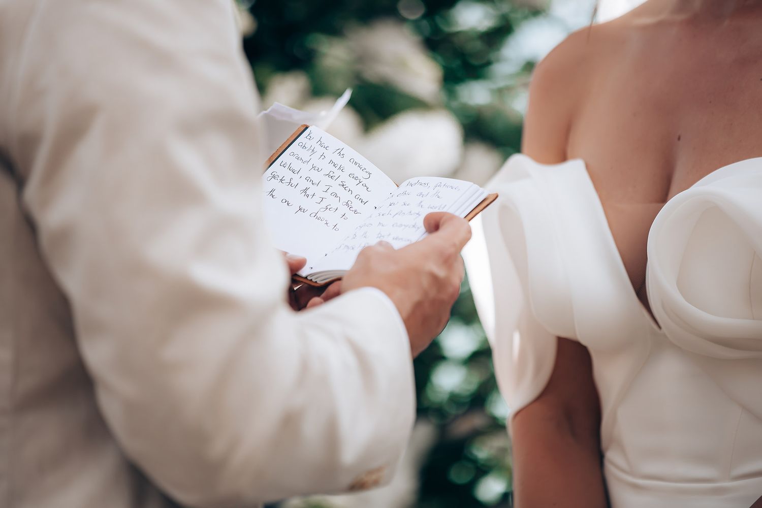 Hands hold a handwritten letter outdoors with trees and sunlight in the background.