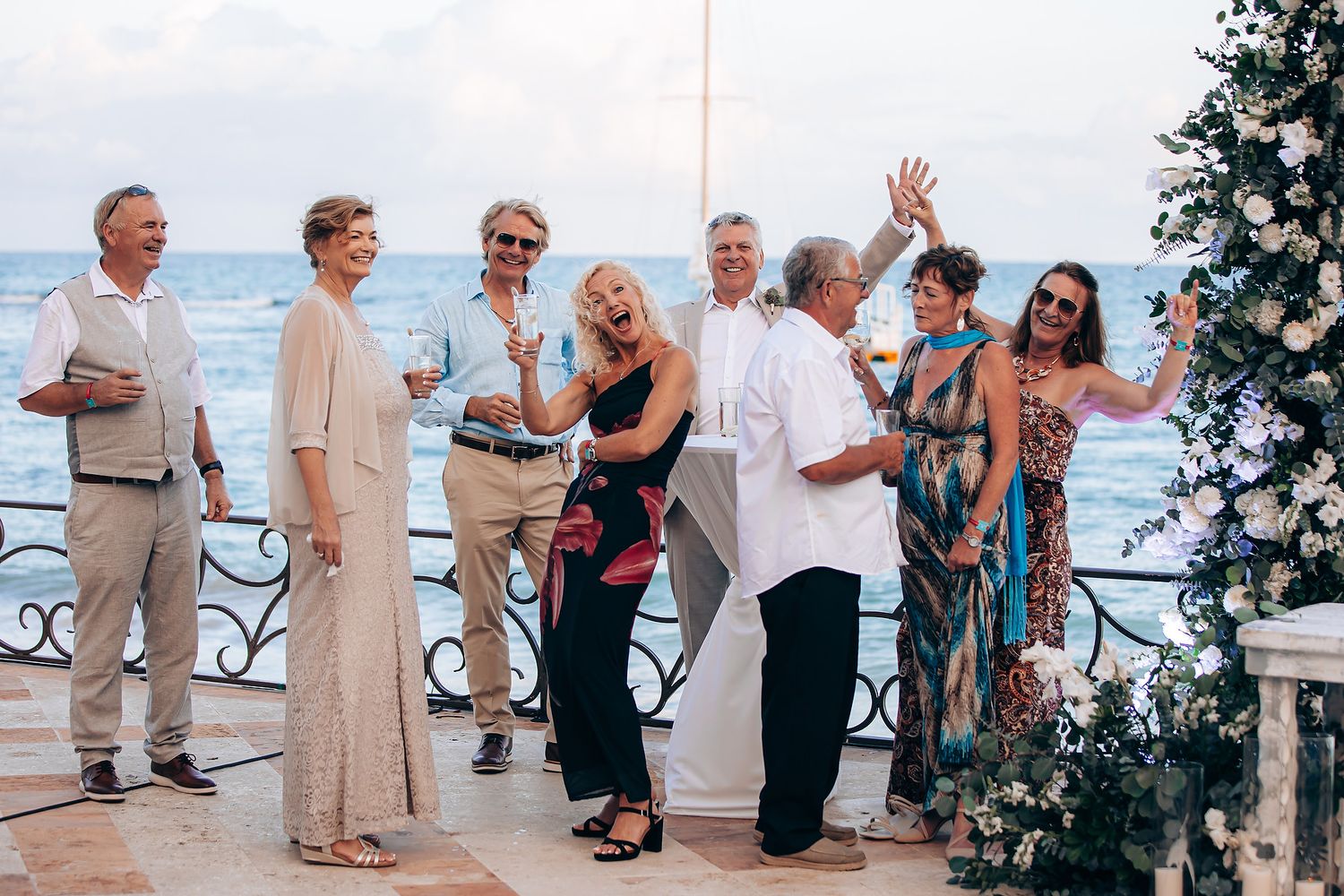 A group of people dancing and celebrating at an outdoor beach wedding reception with ocean views.