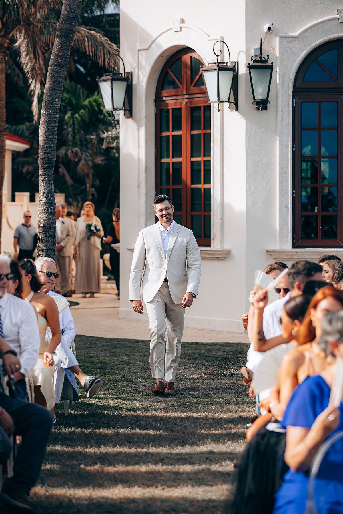 Wedding ceremony setup outdoors with guests seated and Spanish colonial style architecture in background.