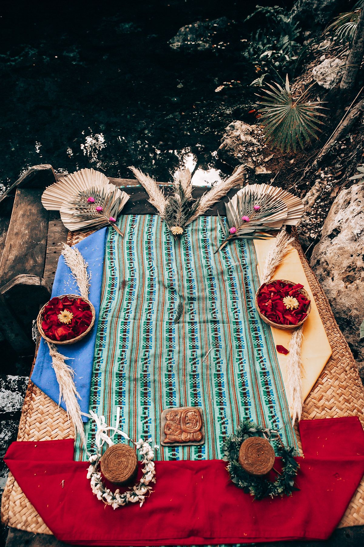 Boho picnic setup with turquoise striped blanket, red cushions, and decorative woven elements on natural ground.