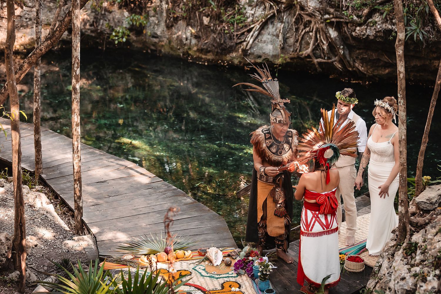 Mayan ceremony wedding at a cenote with officiant in traditional headdress and colorful altar in Mexico.
