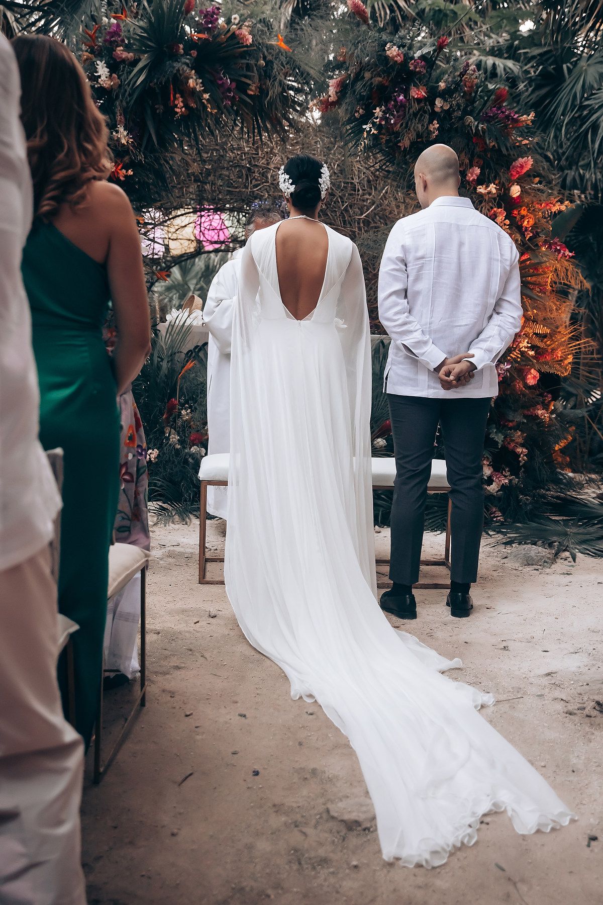 Elegant backless wedding gown with flowing train against tropical garden backdrop.