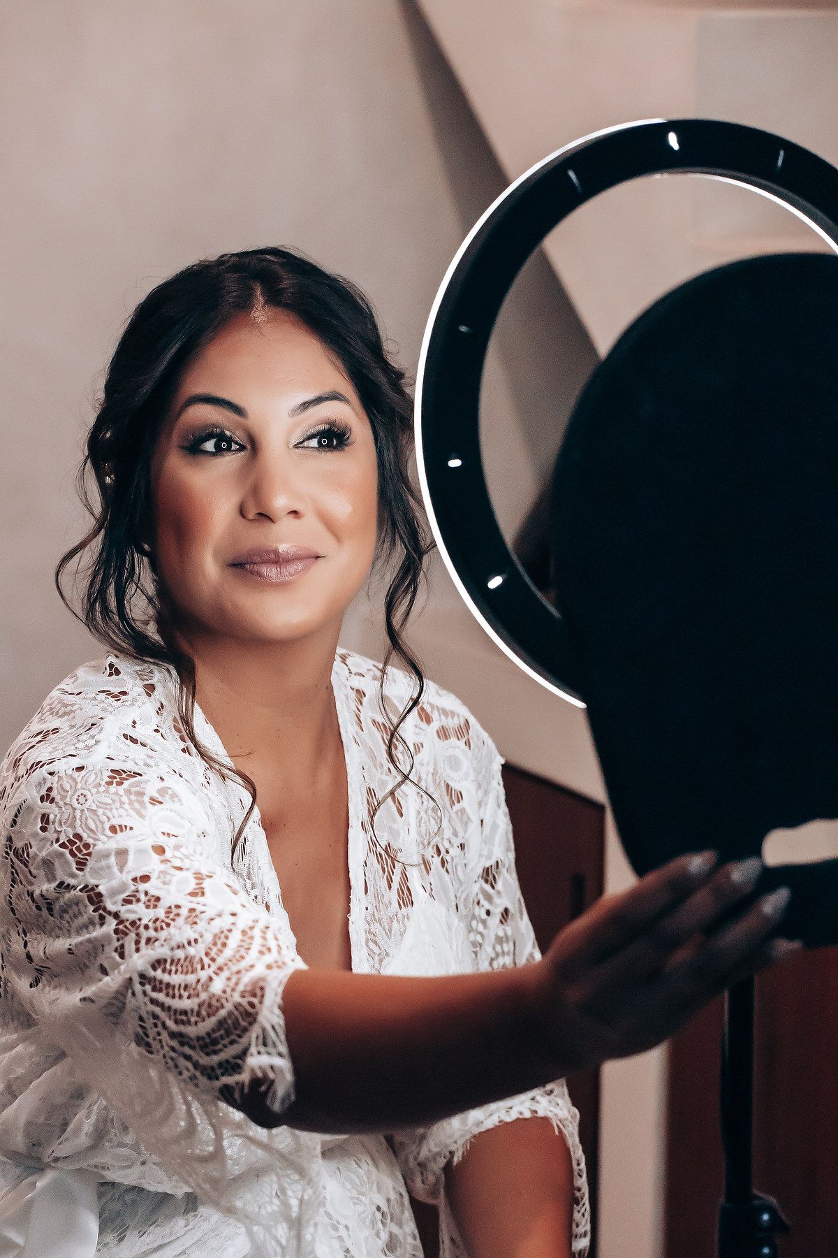A person in a white lace robe poses next to a ring light during wedding preparations.