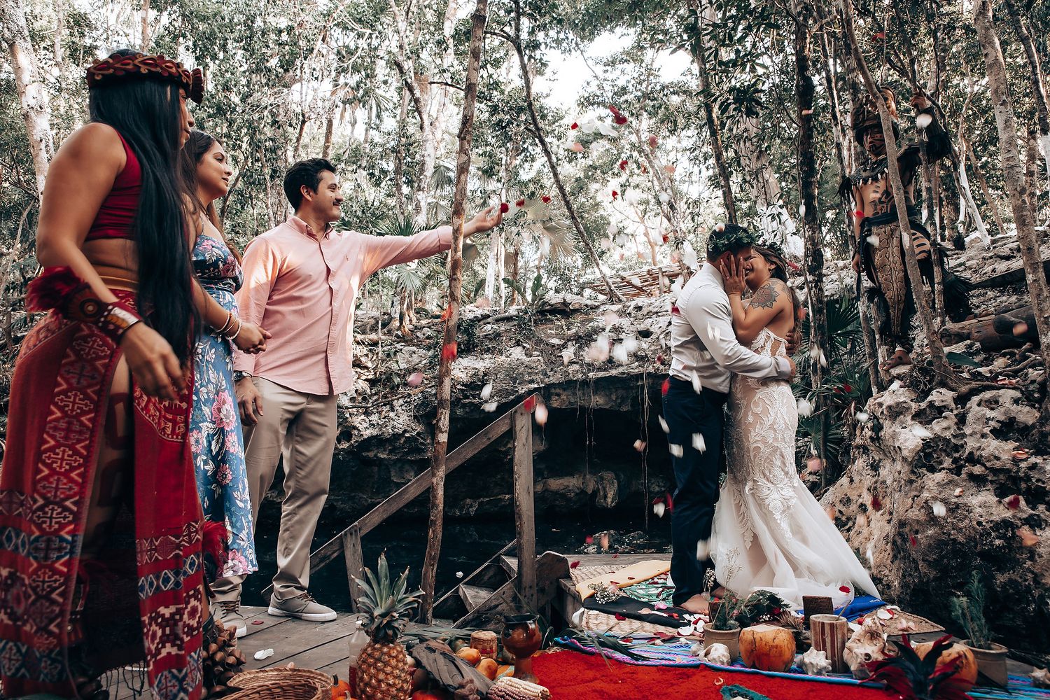Rustic outdoor wedding scene with guests gathered on blankets among trees.