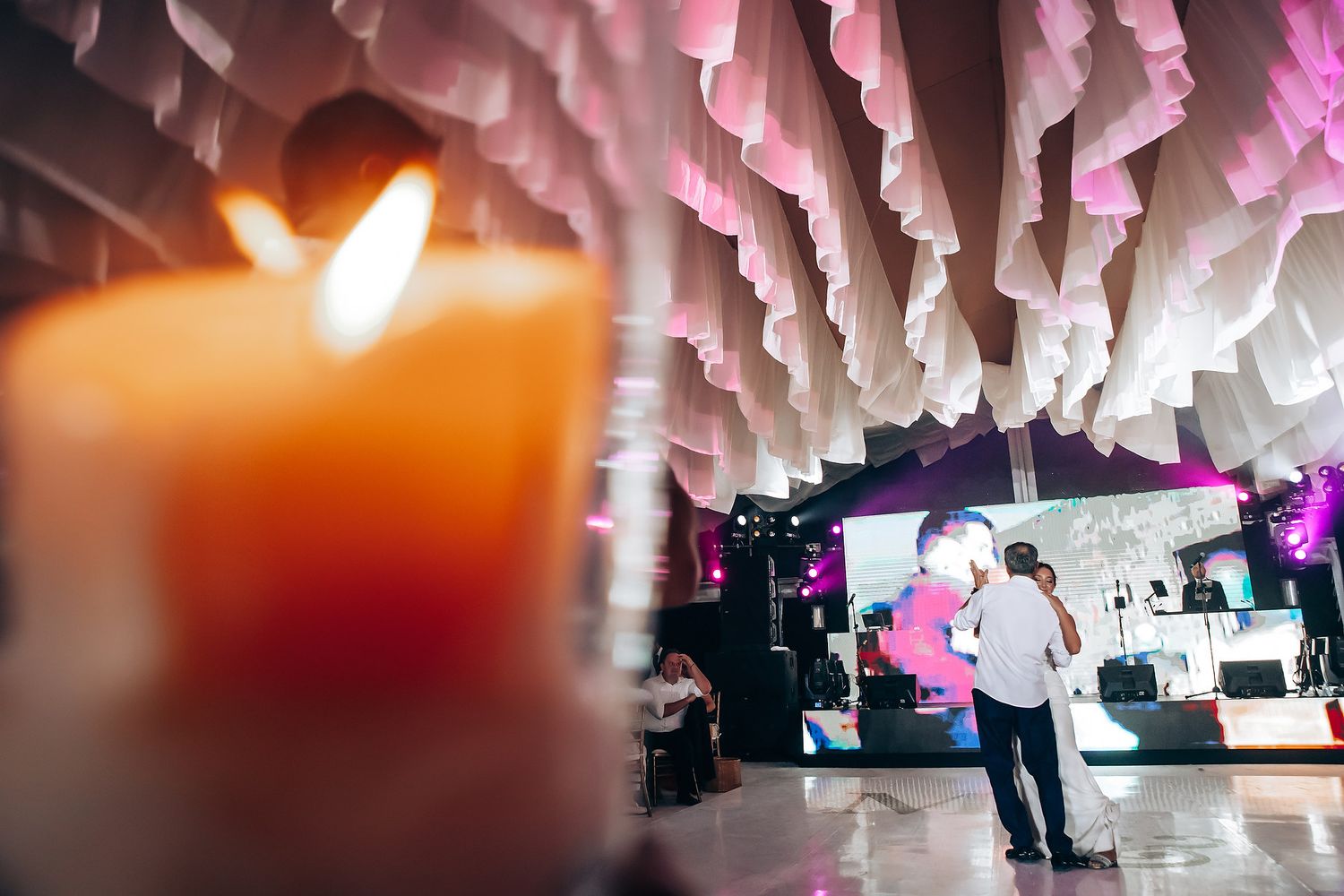 Abstract view of wedding reception decor with pink lighting and hanging white fabric installations.