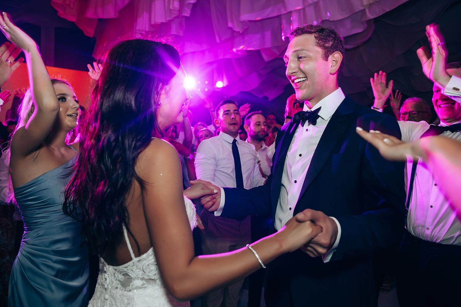 Wedding celebration with vibrant purple lighting and guests dancing on crowded dance floor.