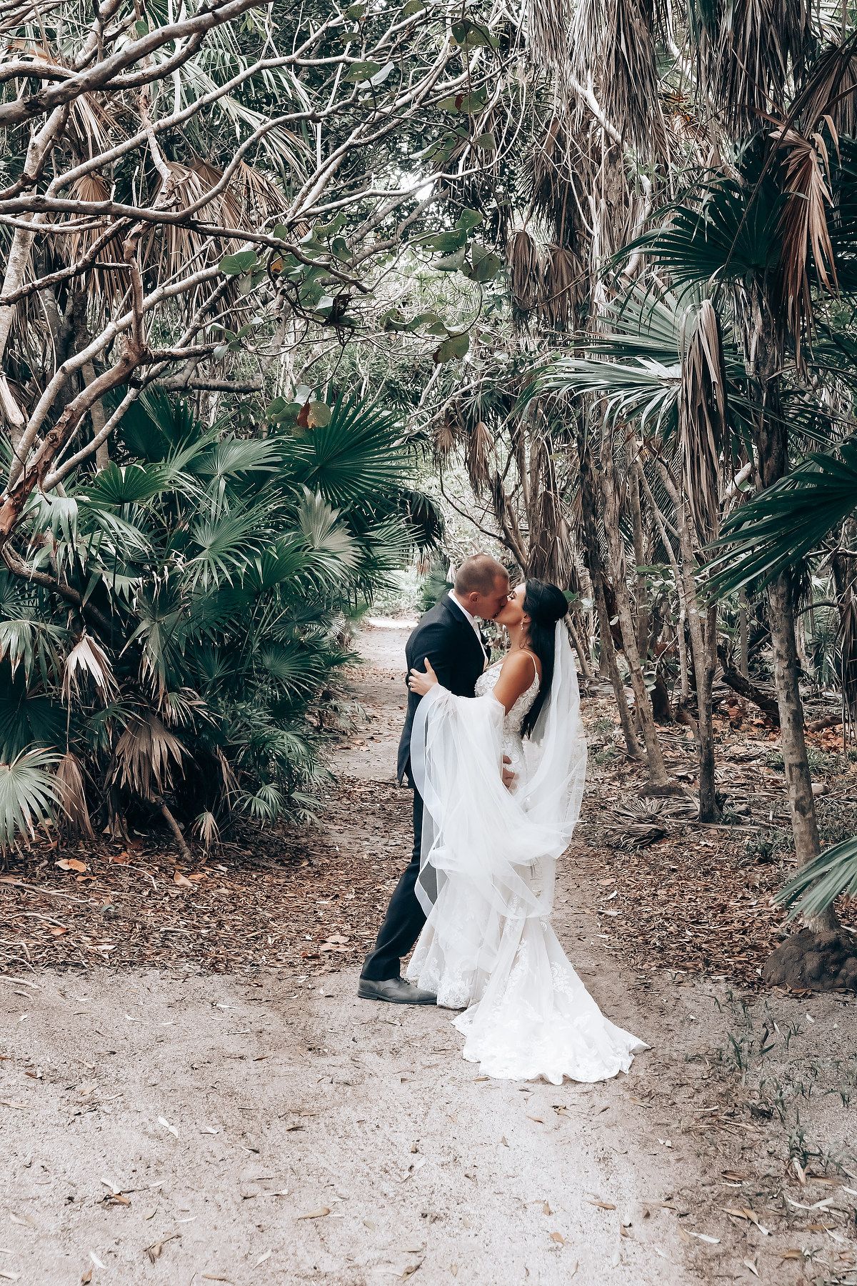 Couple taking romantic photos among palm trees and tropical foliage at a destination wedding.
