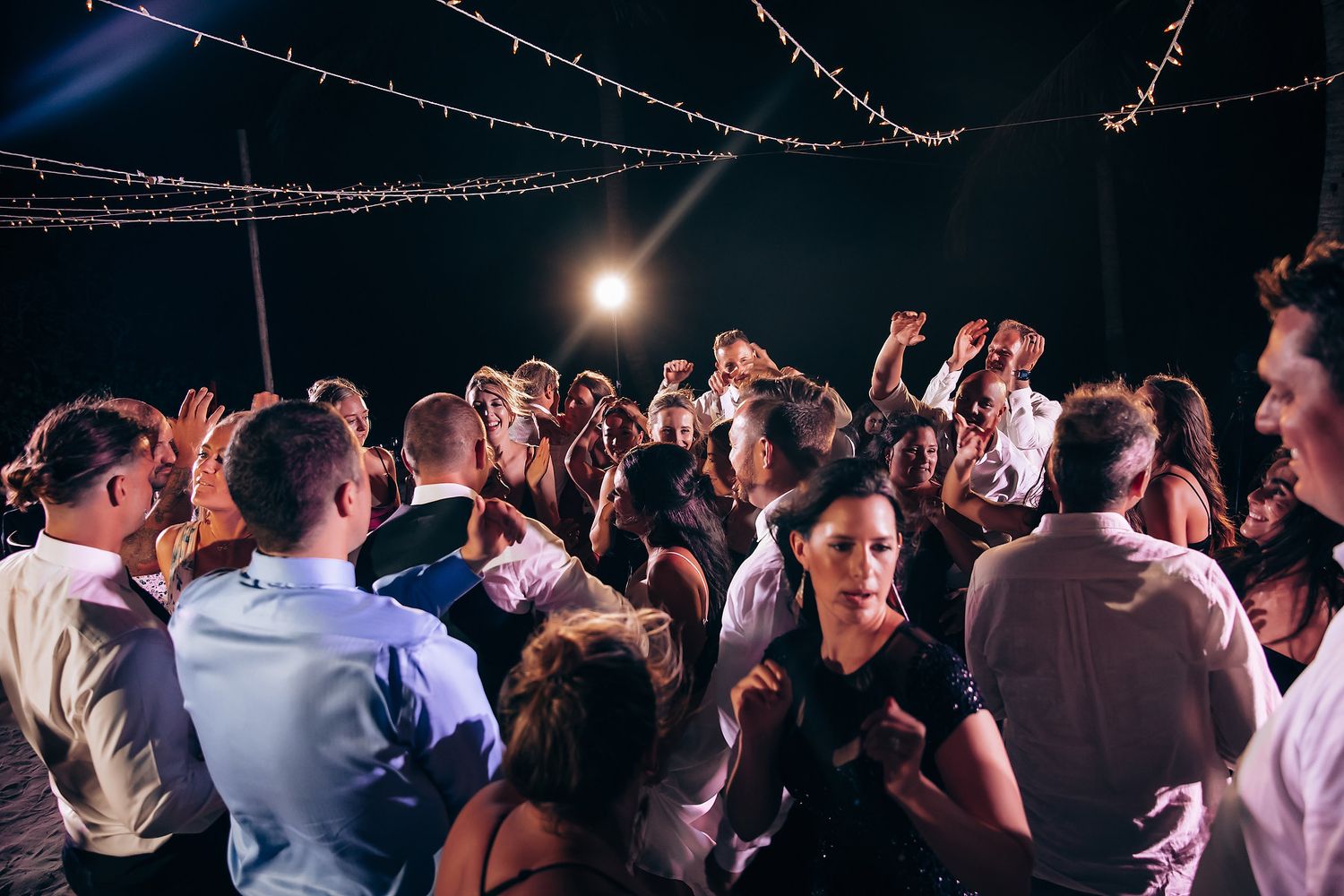 Wedding reception dance party at night with string lights creating a magical atmosphere.