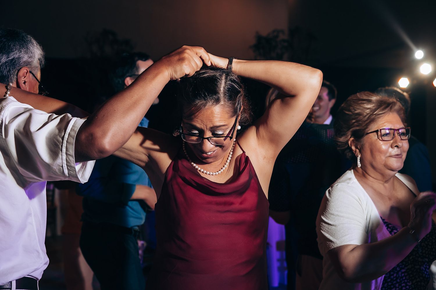Wedding guests dance energetically on the dance floor during an evening reception celebration.