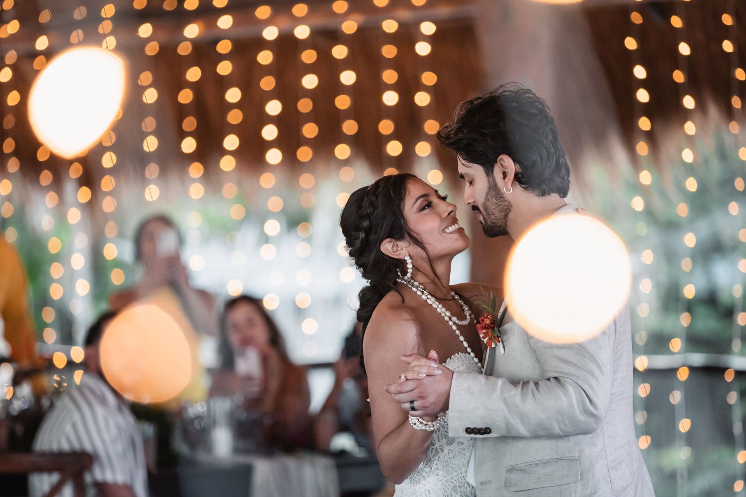 Bride and groom share romantic first dance surrounded by warm glowing bokeh lights at tropical wedding reception.