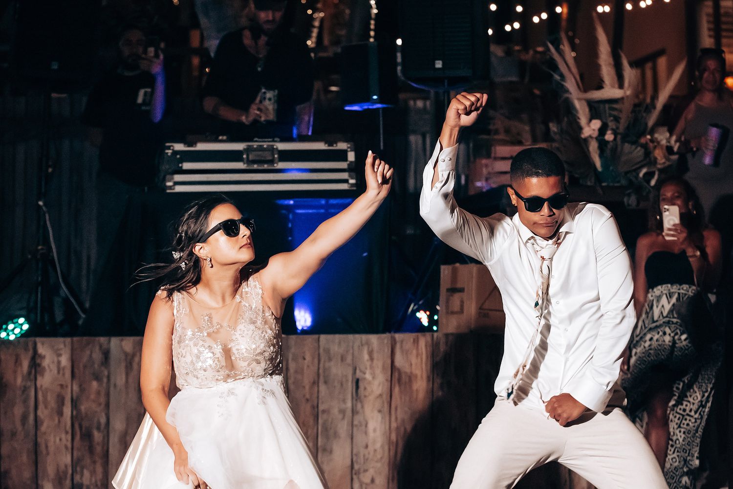 Lively nighttime wedding reception with dancing under rustic wooden beams and string lights.