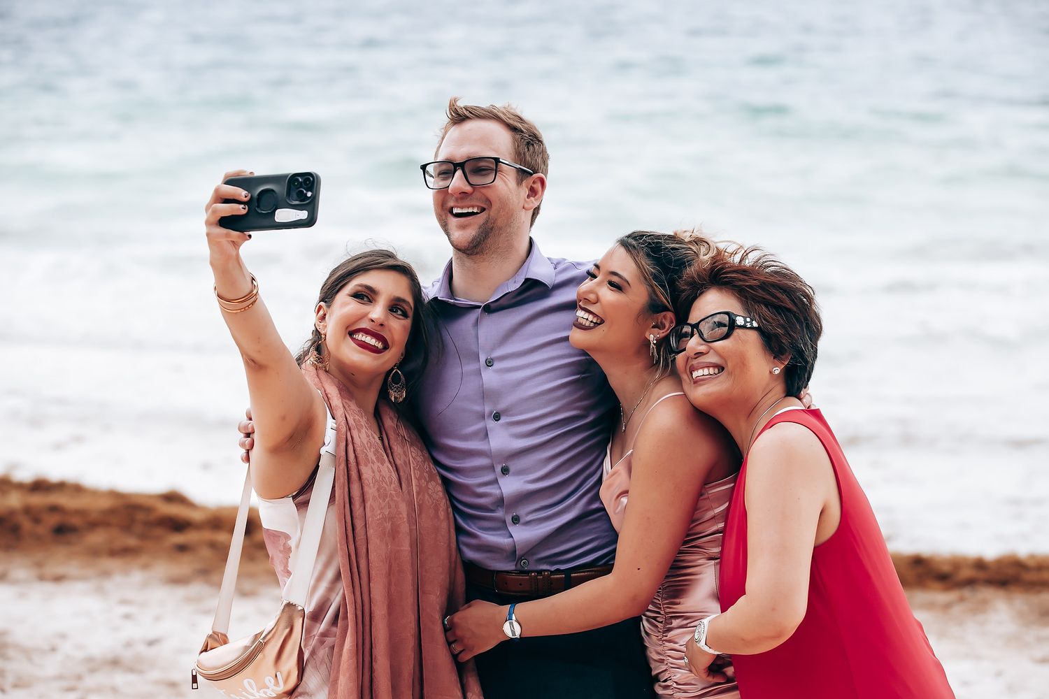 Friends taking selfies and laughing together on a sunny beach.