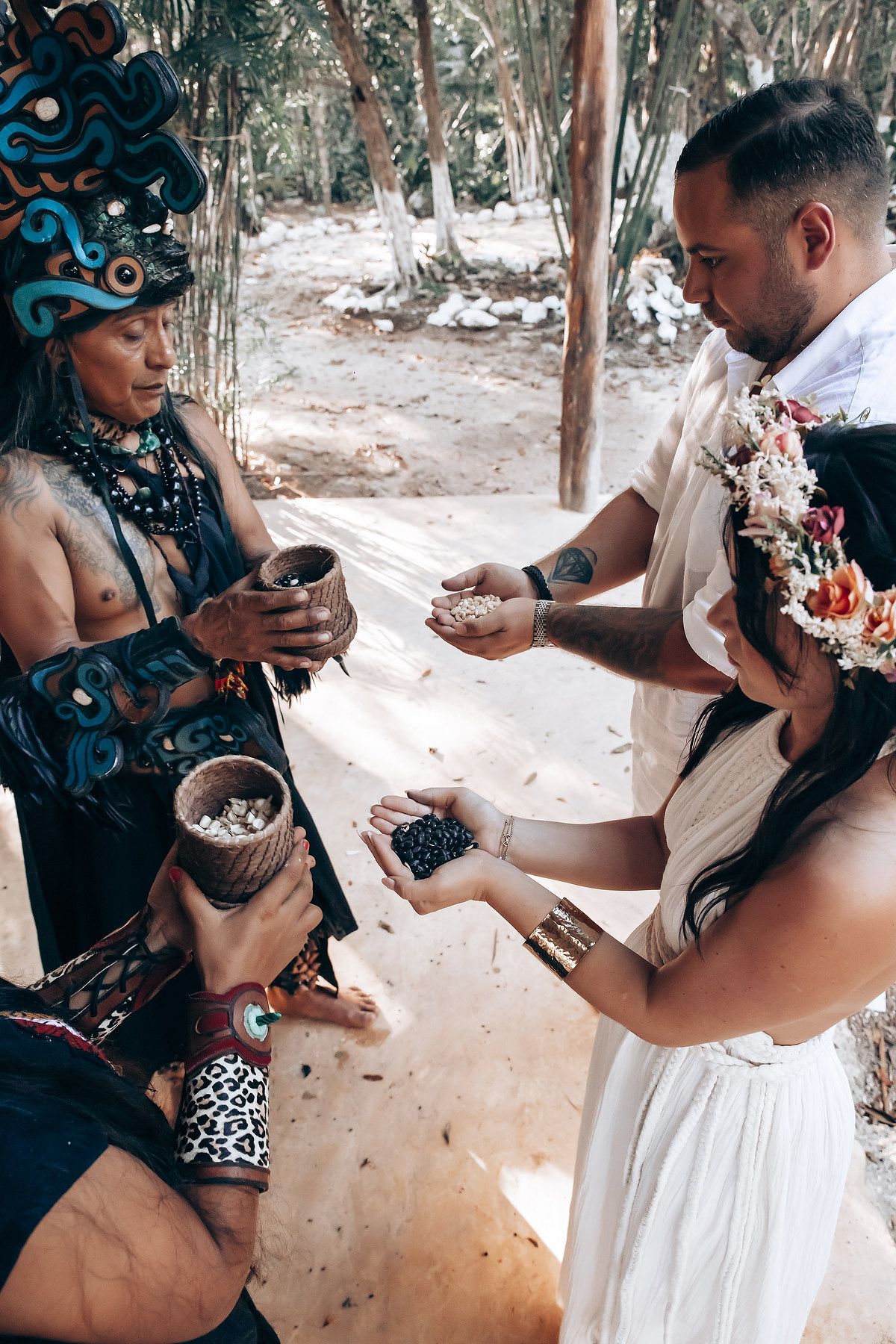 People in traditional dress share ceremonial offerings during an outdoor ritual.