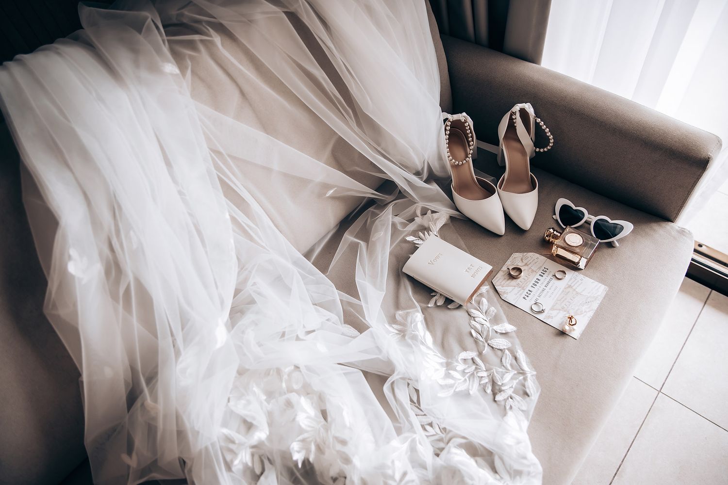 A wedding dress hangs elegantly against a white wall, showcasing its intricate lace details and flowing silhouette.