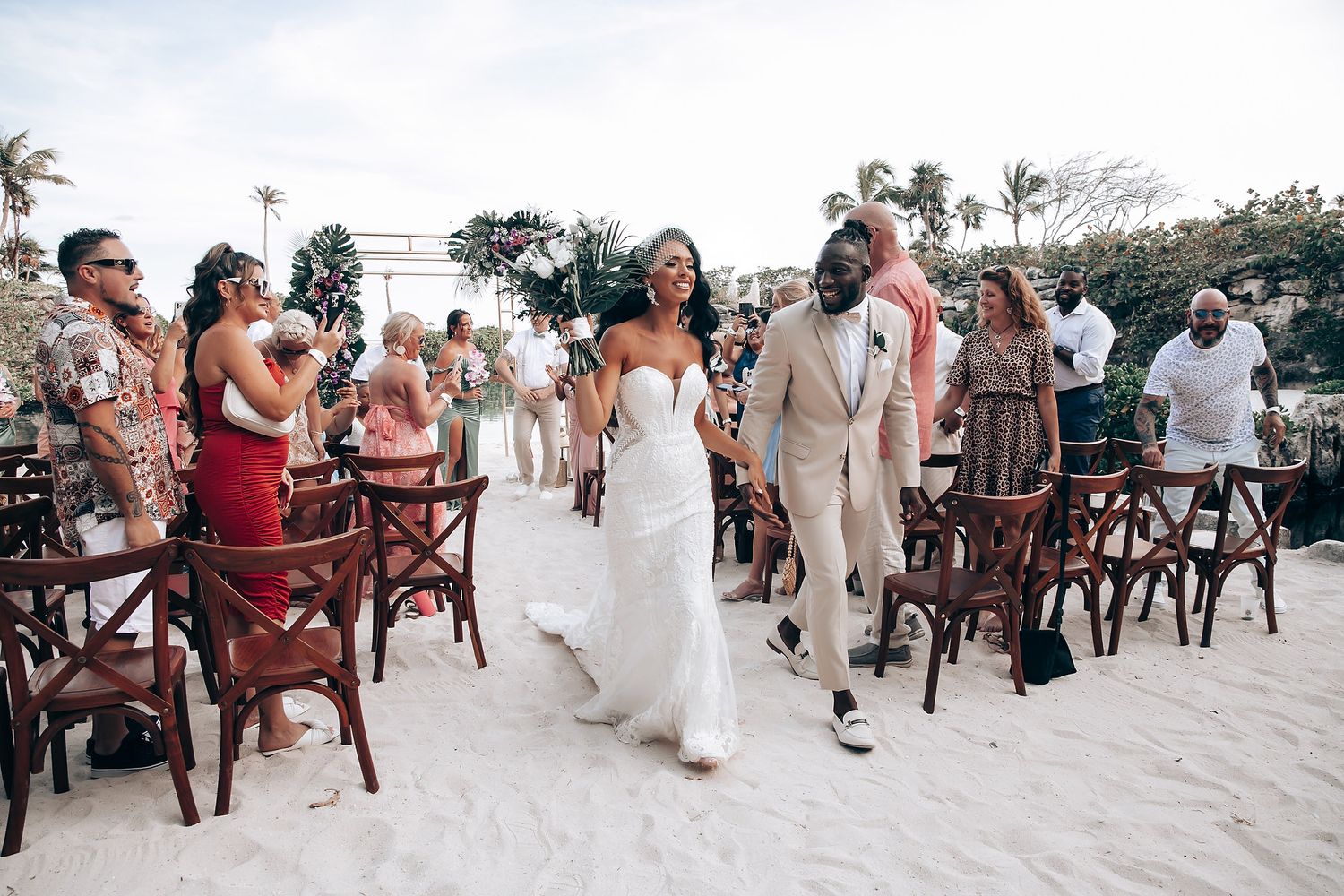 Wedding ceremony setup on a white sandy beach with guests in attendance.
