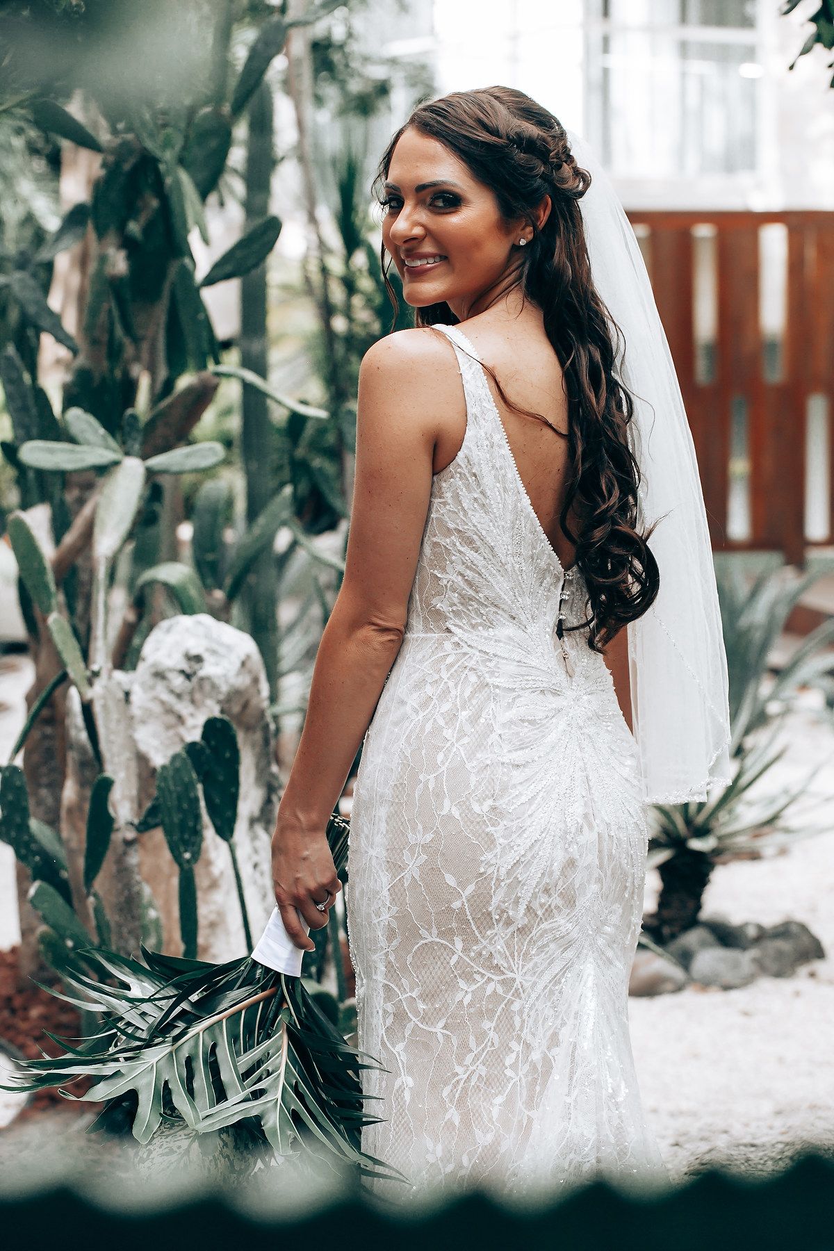 Elegant lace wedding dress with intricate details shown from behind against a tropical garden backdrop.
