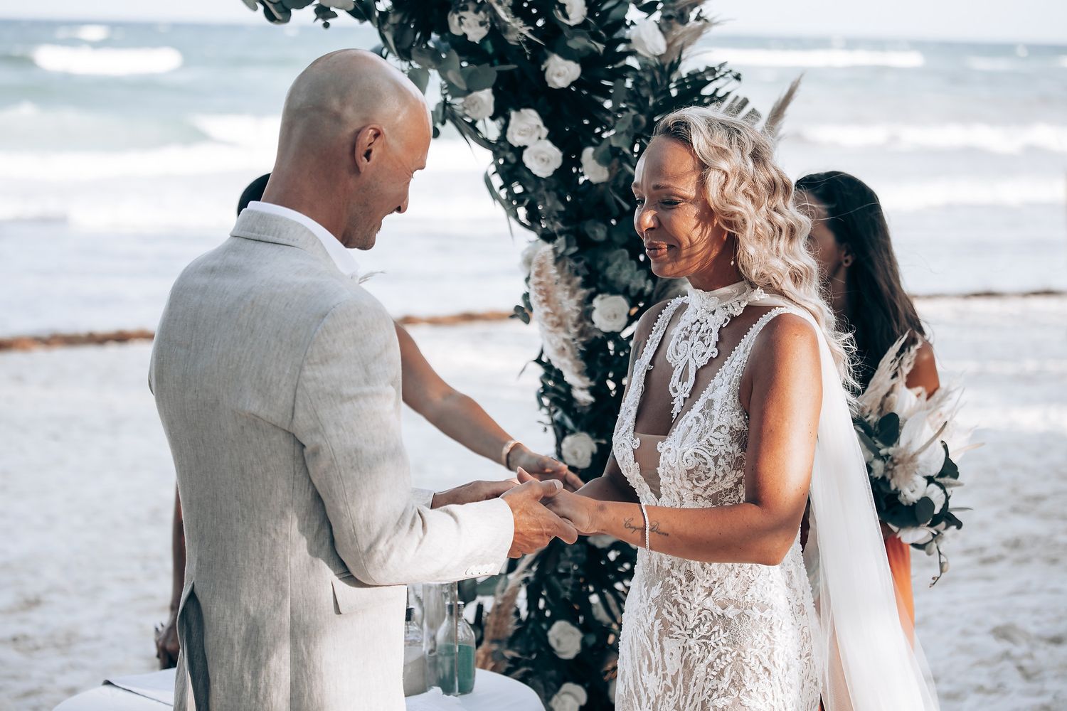 A beach wedding scene with waves and floral decorations in the background.