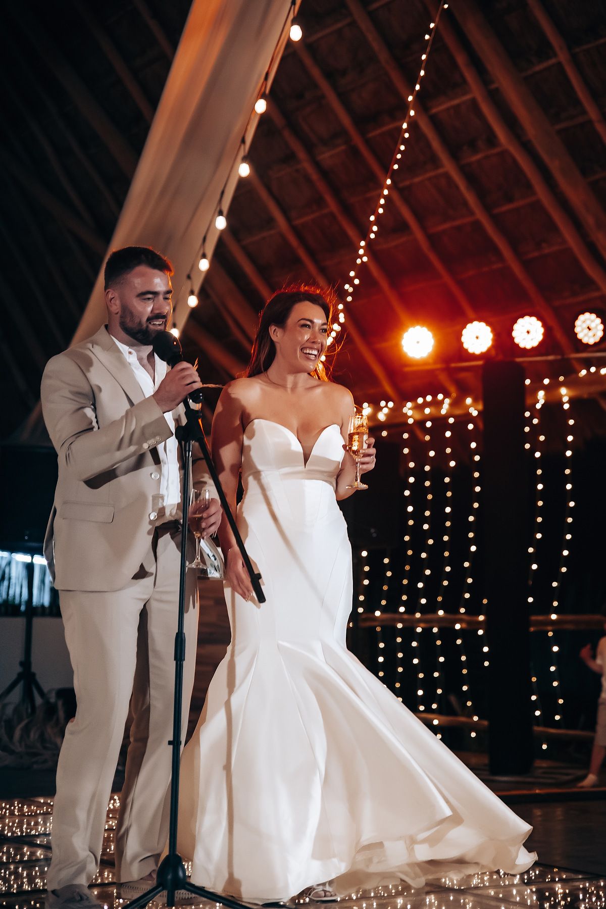 A couple shares a romantic dance moment under twinkling lights at their wedding reception in a rustic barn venue.