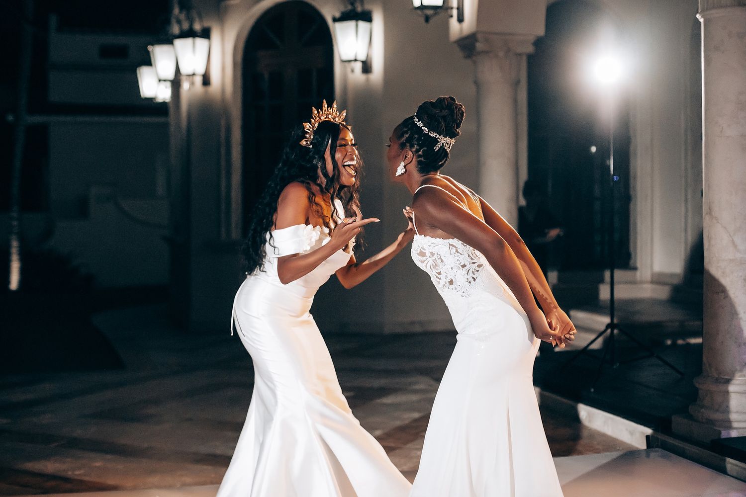 Wedding party dancing and celebrating in an elegant hallway with dramatic lighting.
