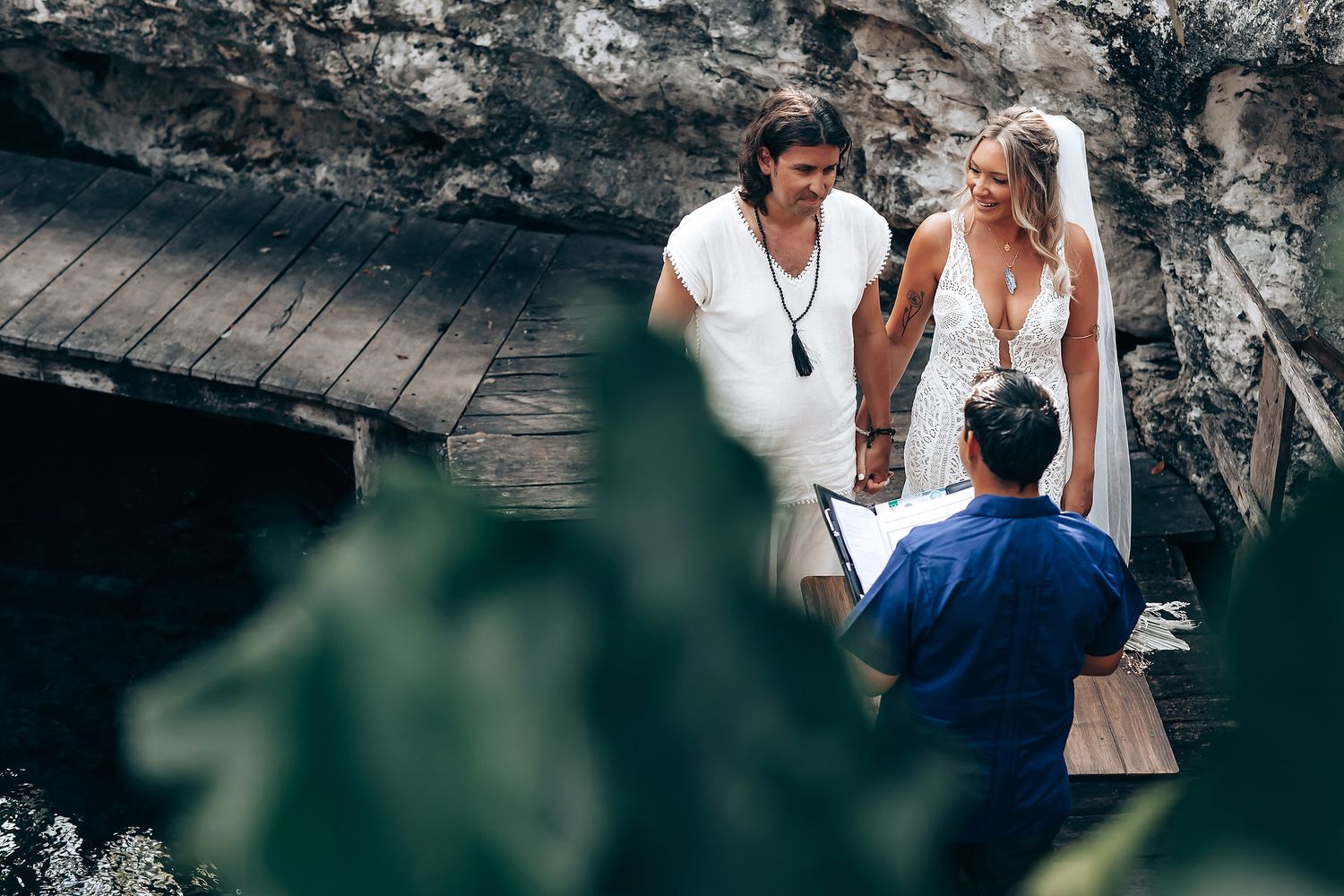 A couple shares an intimate moment in a natural setting surrounded by dramatic rocky cliffs and greenery.