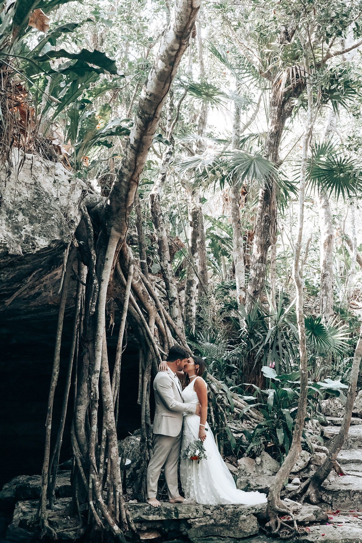 A couple shares an intimate moment in a secluded forest setting surrounded by palm trees and natural greenery.
