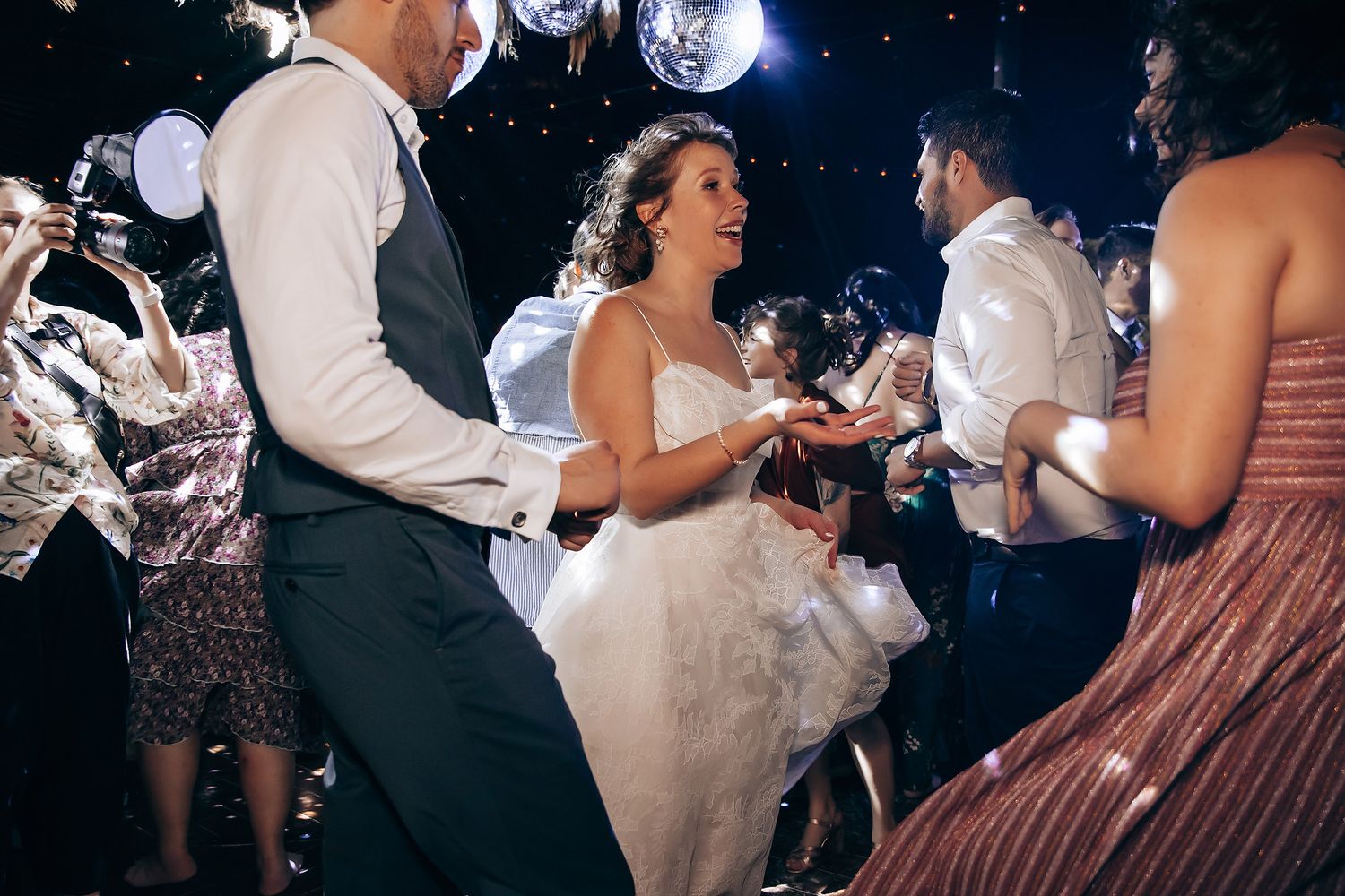 Wedding reception dance floor filled with guests celebrating under disco balls and string lights.
