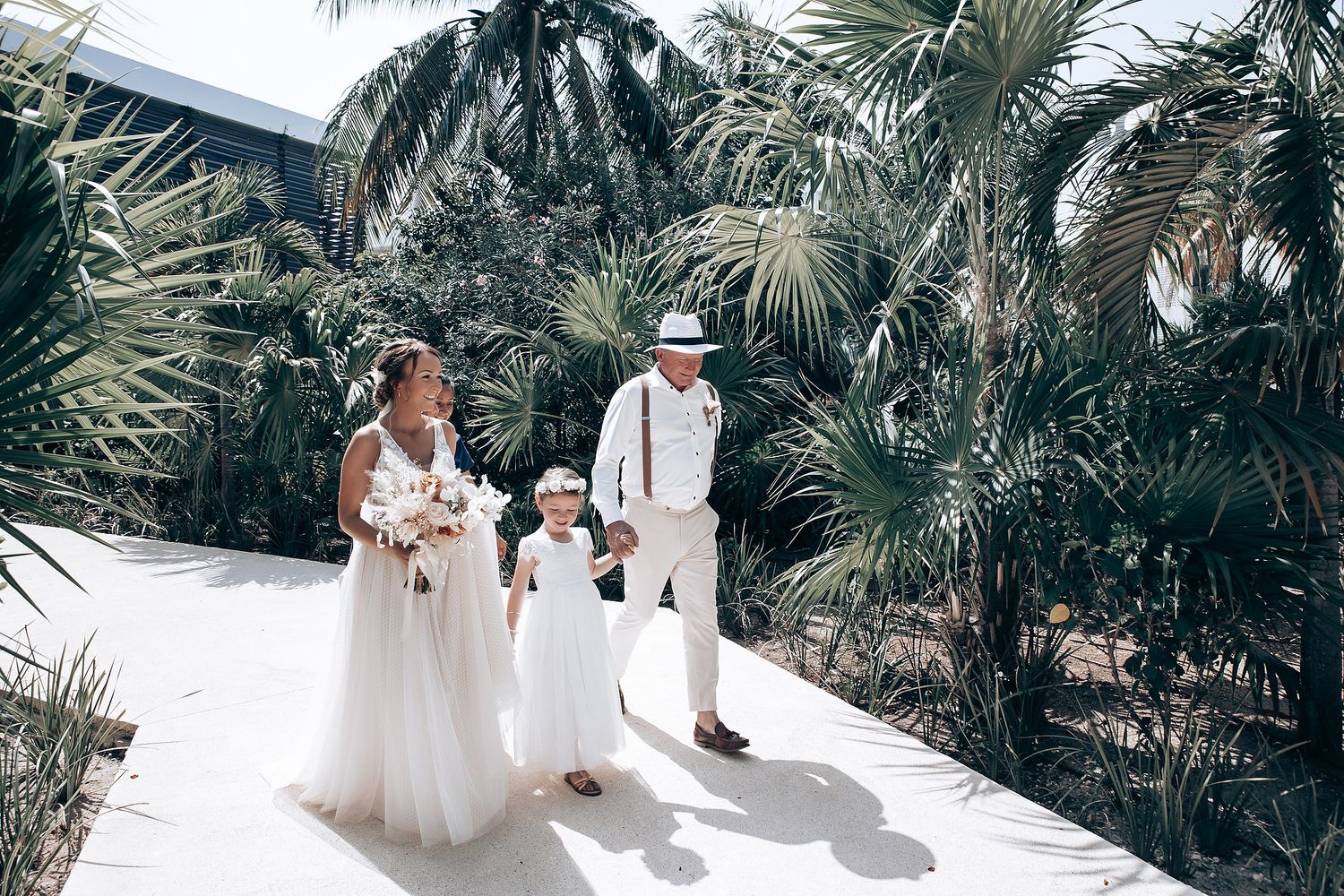 Tropical beach wedding setup with palm trees and white decor on sandy shore.