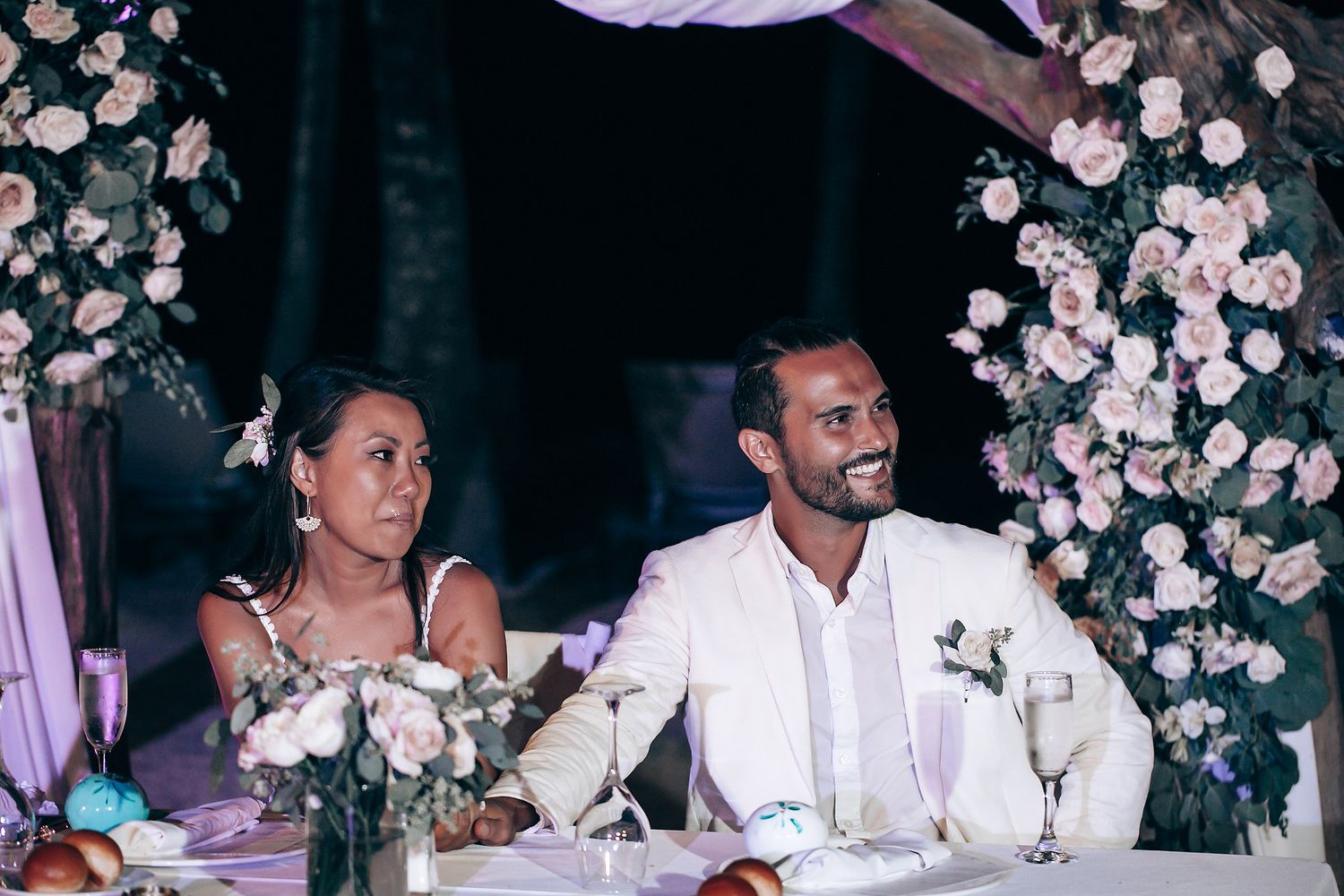 Wedding reception table decorated with pink floral arrangements and purple lighting.