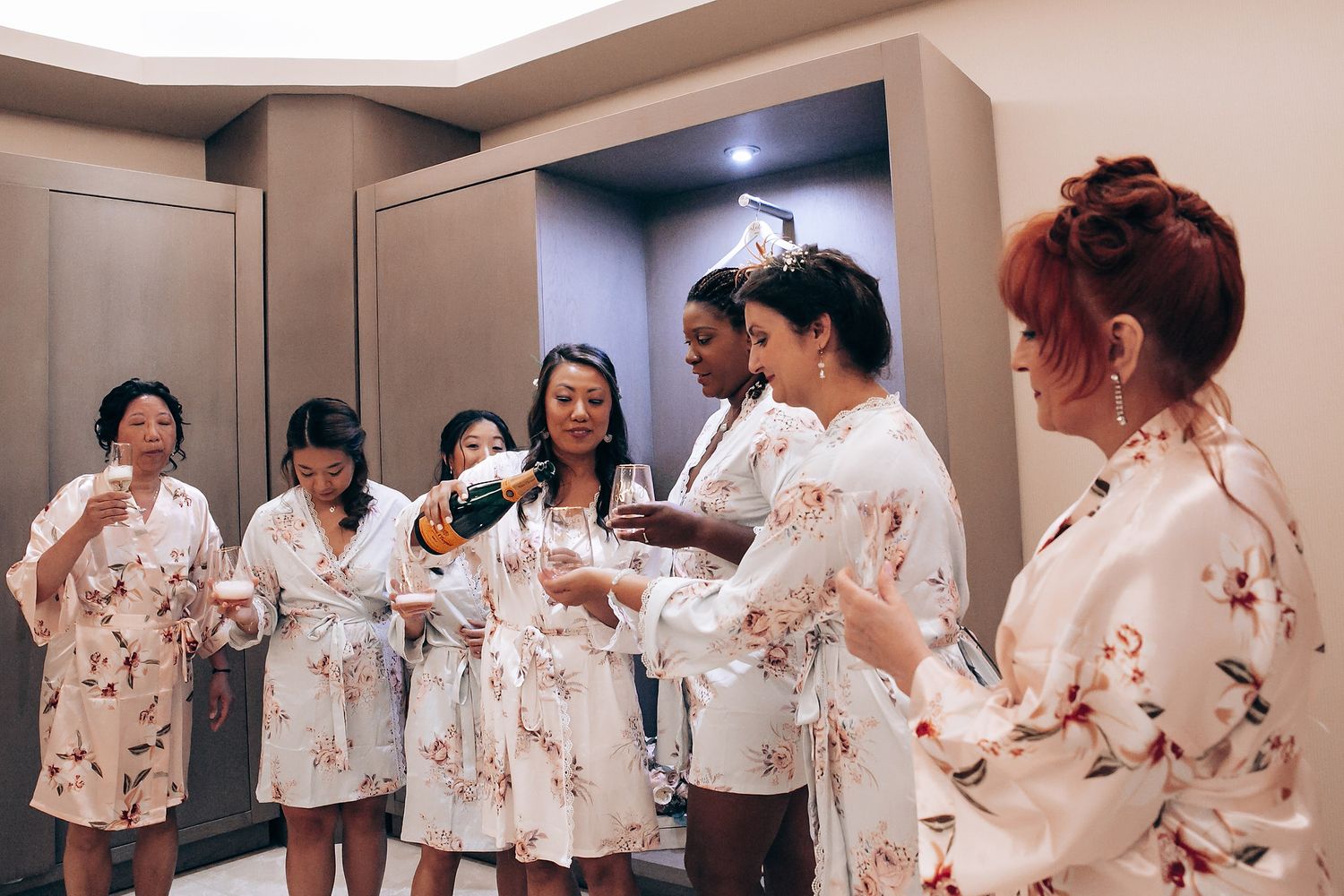 Wedding party members in matching floral robes pose together in a bright indoor space.