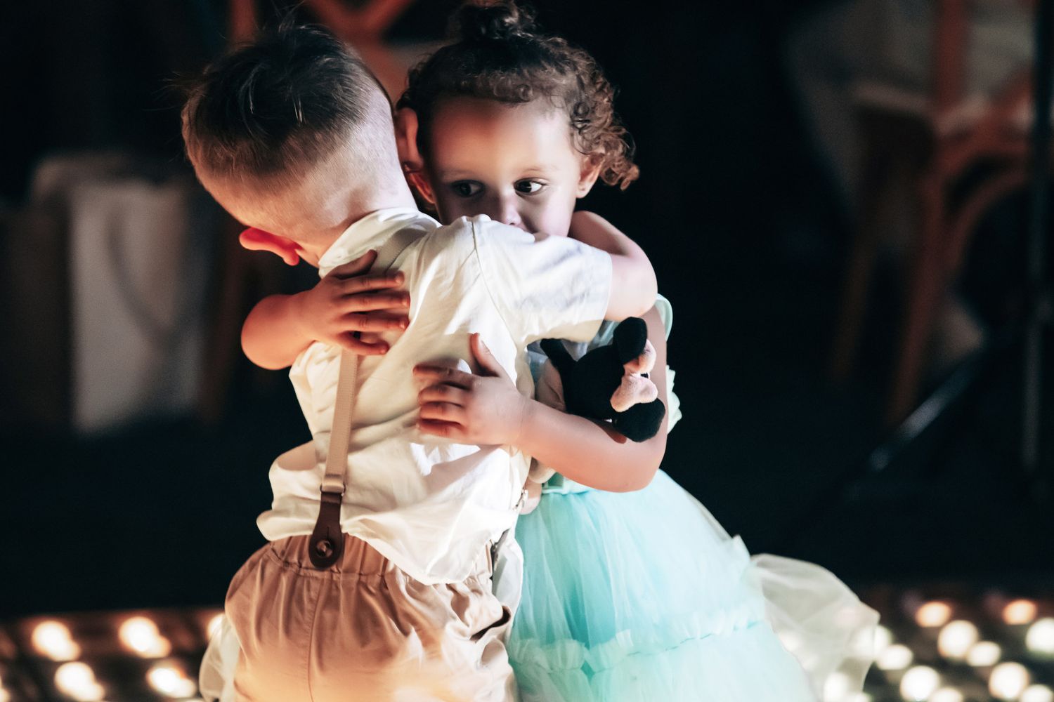 Two young children share a sweet hug on a dance floor at a wedding reception.
