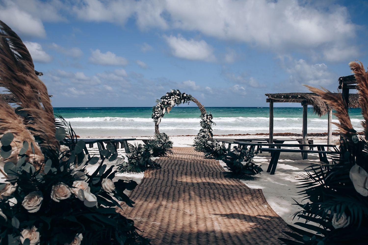Panoramic view of a beach wedding setup with chairs and ocean backdrop under blue skies.