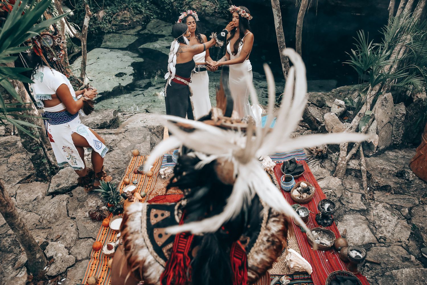 Tropical beach wedding ceremony setup with white decor and palm trees along a rocky coastline.