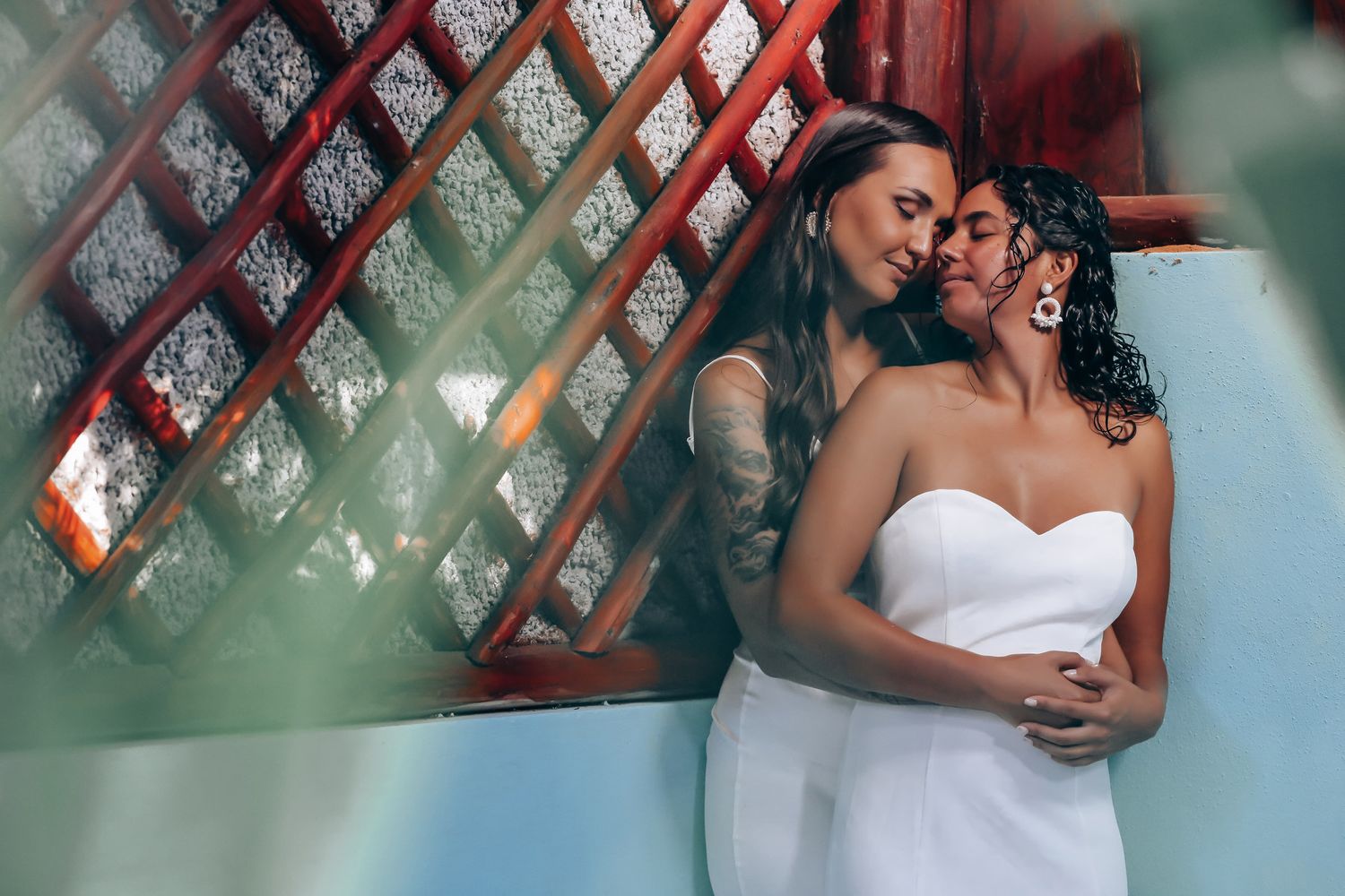 Intimate moment captured in front of red-tinted architectural details and greenery.