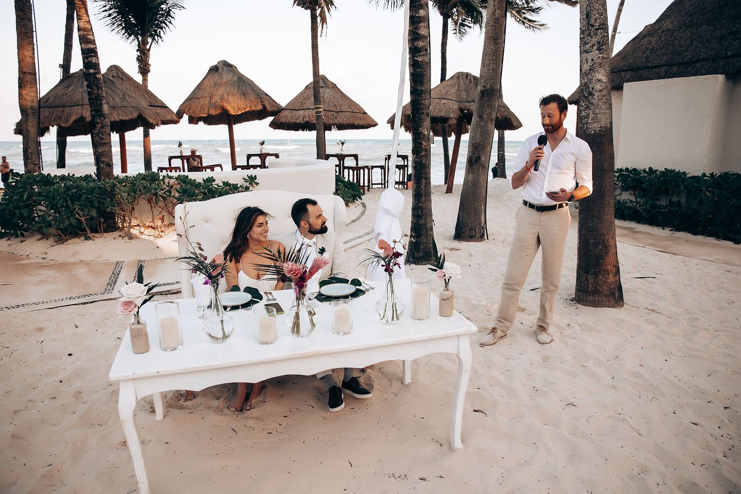 Beachfront wedding reception with white tables and palm trees creating a tropical atmosphere.